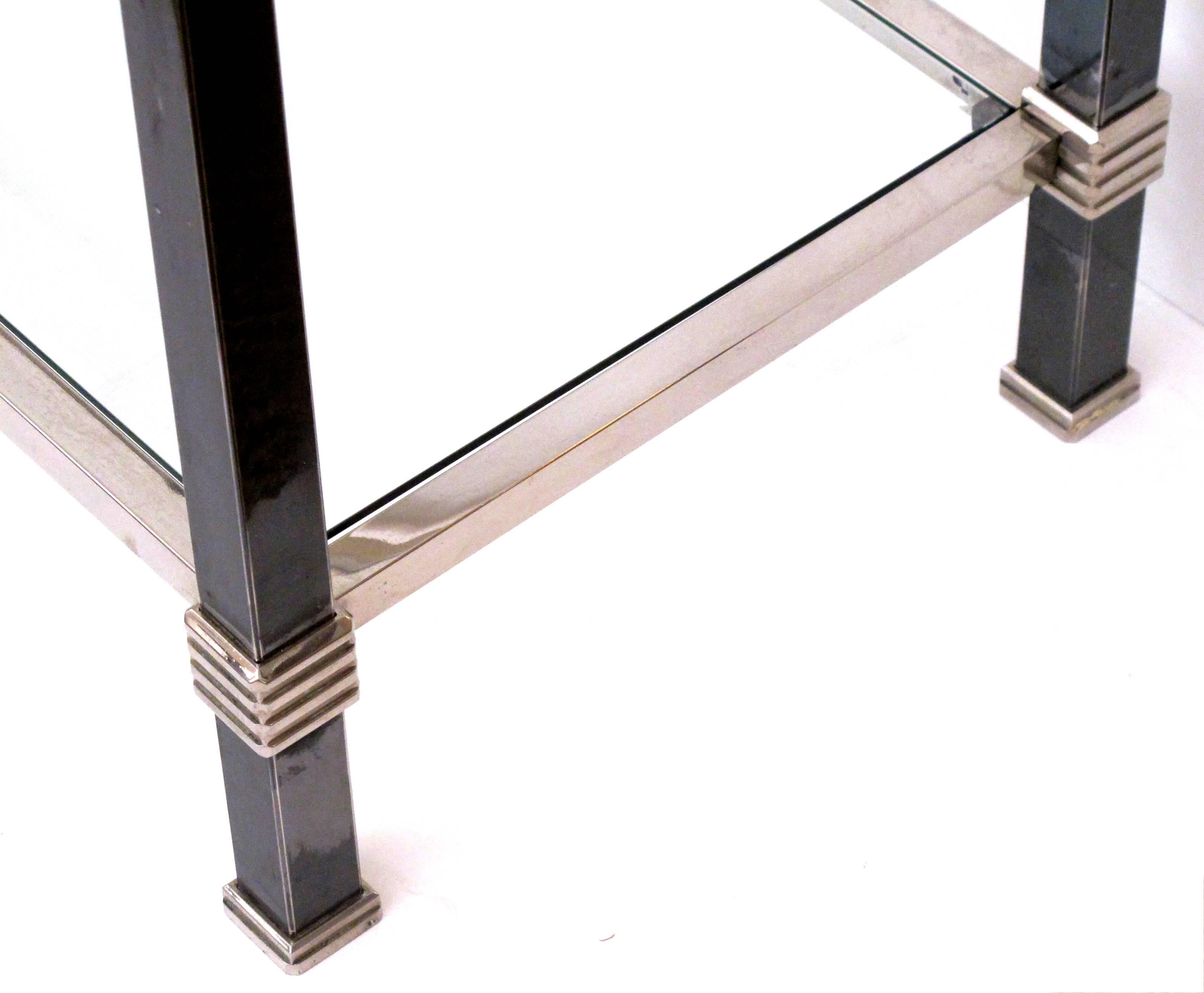 A tailored French 1970s two-toned steel console table with beveled glass top and lower shelf; the rectangular top raised on square supports with ribbed caps; all joined by a lower glass shelf.