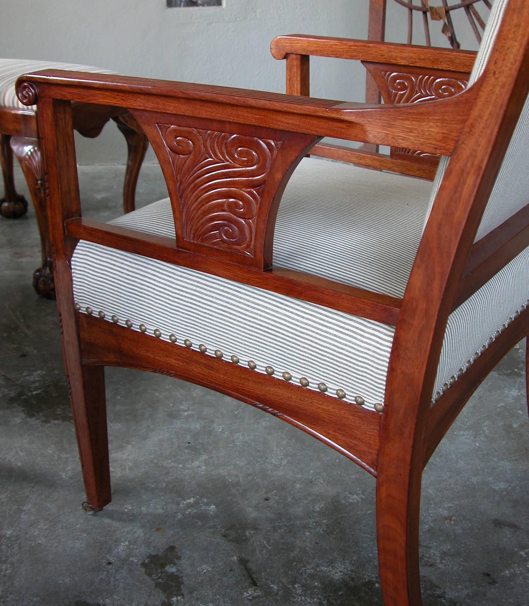 A rare pair of French Art Nouveau carved mahogany armchairs; the gently bowed crest rail with scrolled ends above a padded back and tight seat; flanked by squared open-work arms with scrolling terminals; the arching apron raised on quadrangular