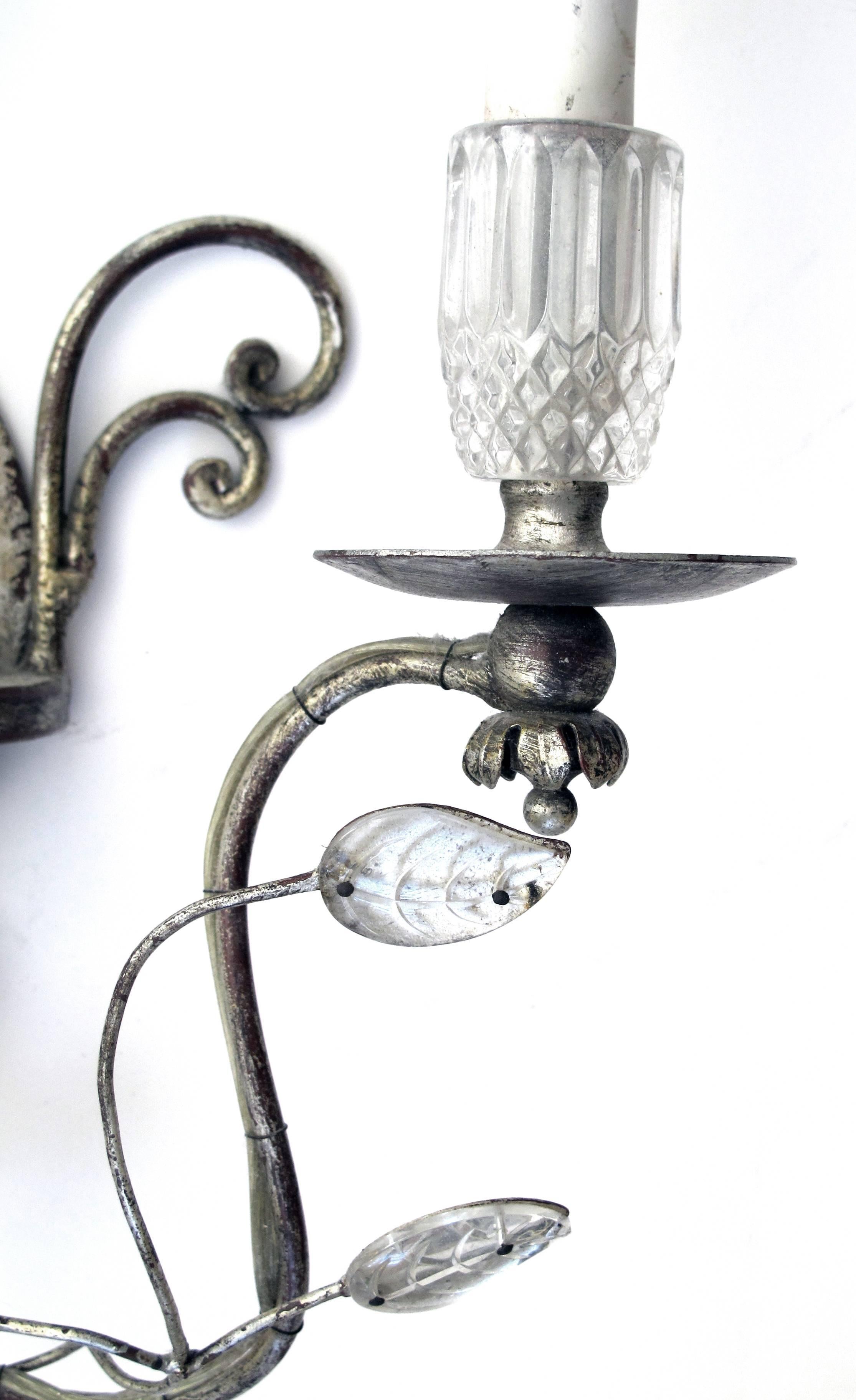 An elegant pair of French Mid-Century Maison Bagues style silver-leafed and glass bird sconces; each opposing glass parrot surrounded by meandering vines with glass leaves and flowers; supporting two scrolling arms with faceted glass candle cups.