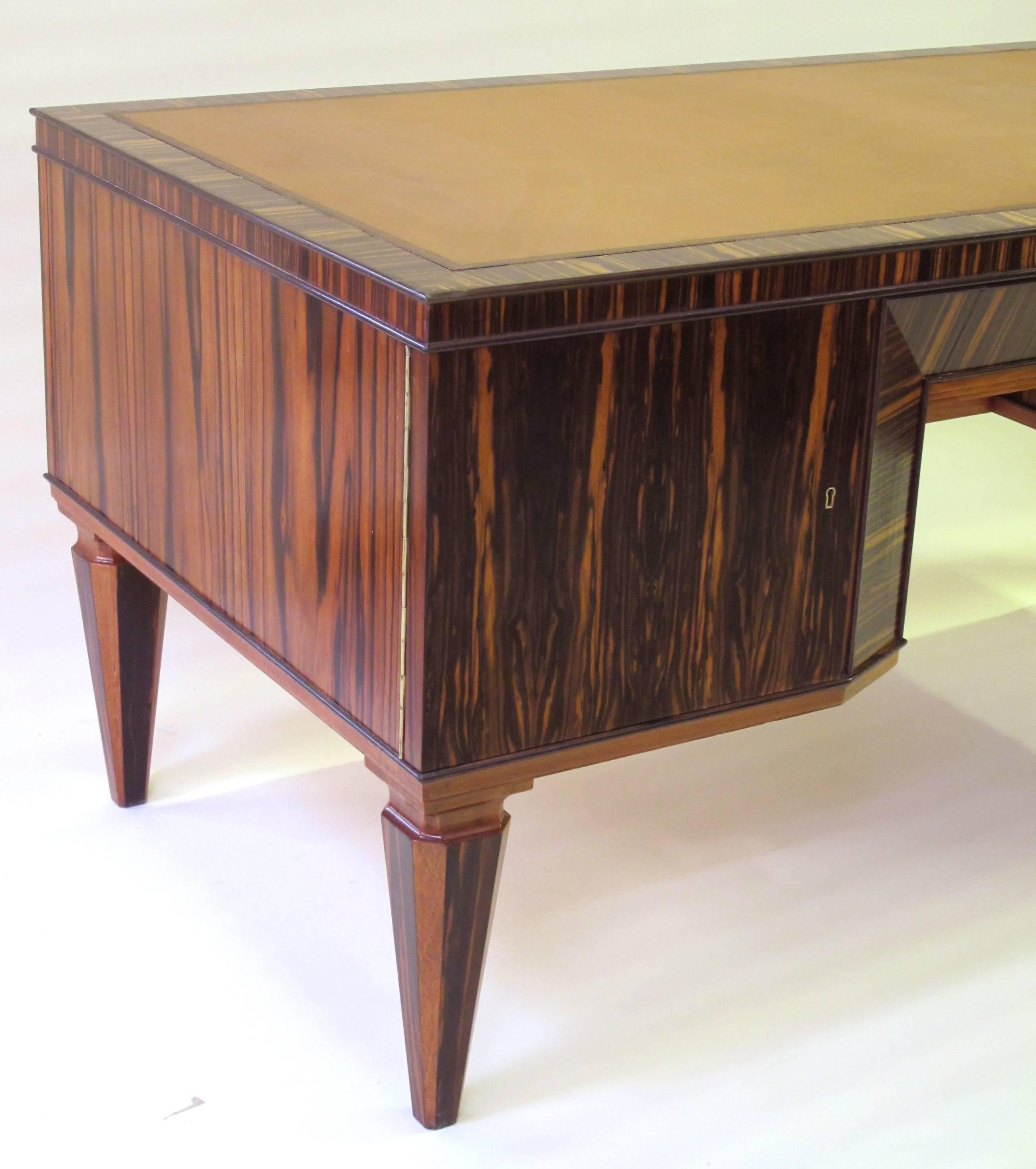 A handsome and boldly-scaled French Art Deco Macassar-veneered pedestal desk; the robustly-proportioned desk with inset hand-tooled leather top above a central drawer flanked by pedestal doors; raised on tapering block supports; new leather top.