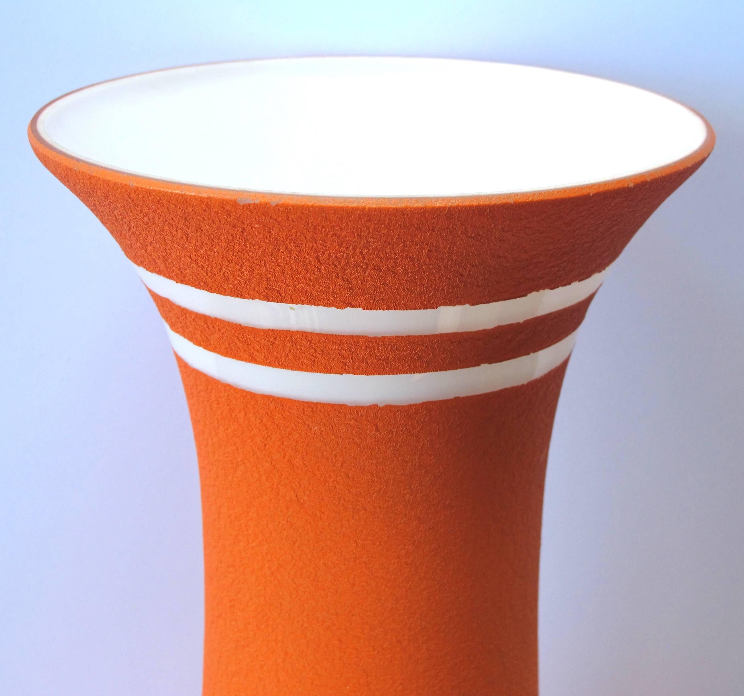 A tall and striking American 1960s orange glazed vase with white ground; the tall vase of white cased-glass covered in an orange textured glaze adorned with a continuous fret band.