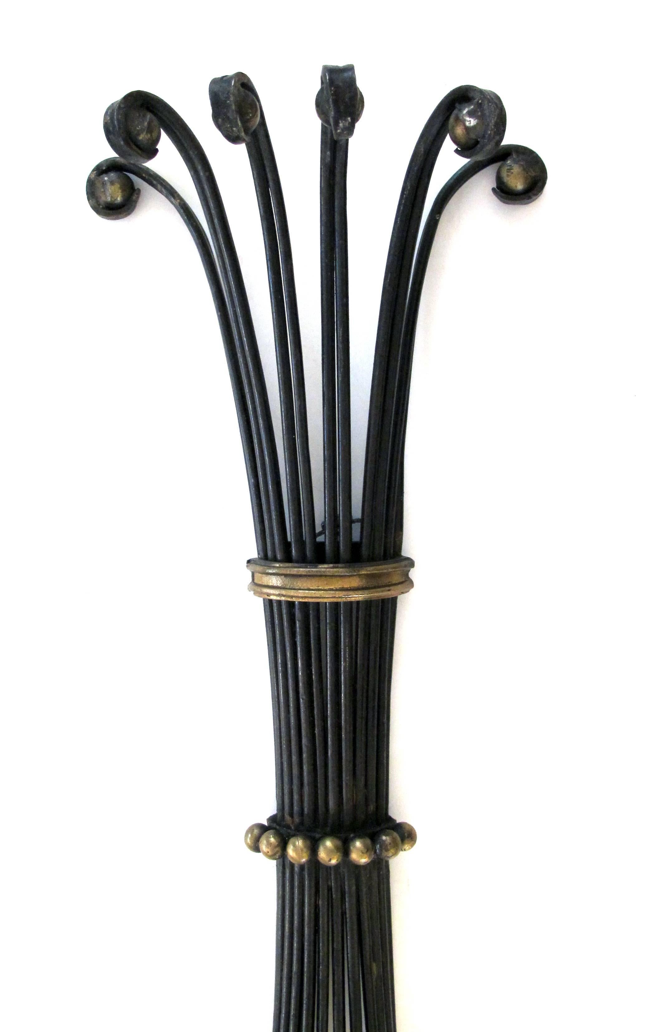 A lyrical and large-scaled pair of American 1960s black painted wrought iron six-arm wall sconces with gilt highlights; each openwork sconce with flaring top; waisted mid-section and graceful up-turned arms with turned wooden candle cups.