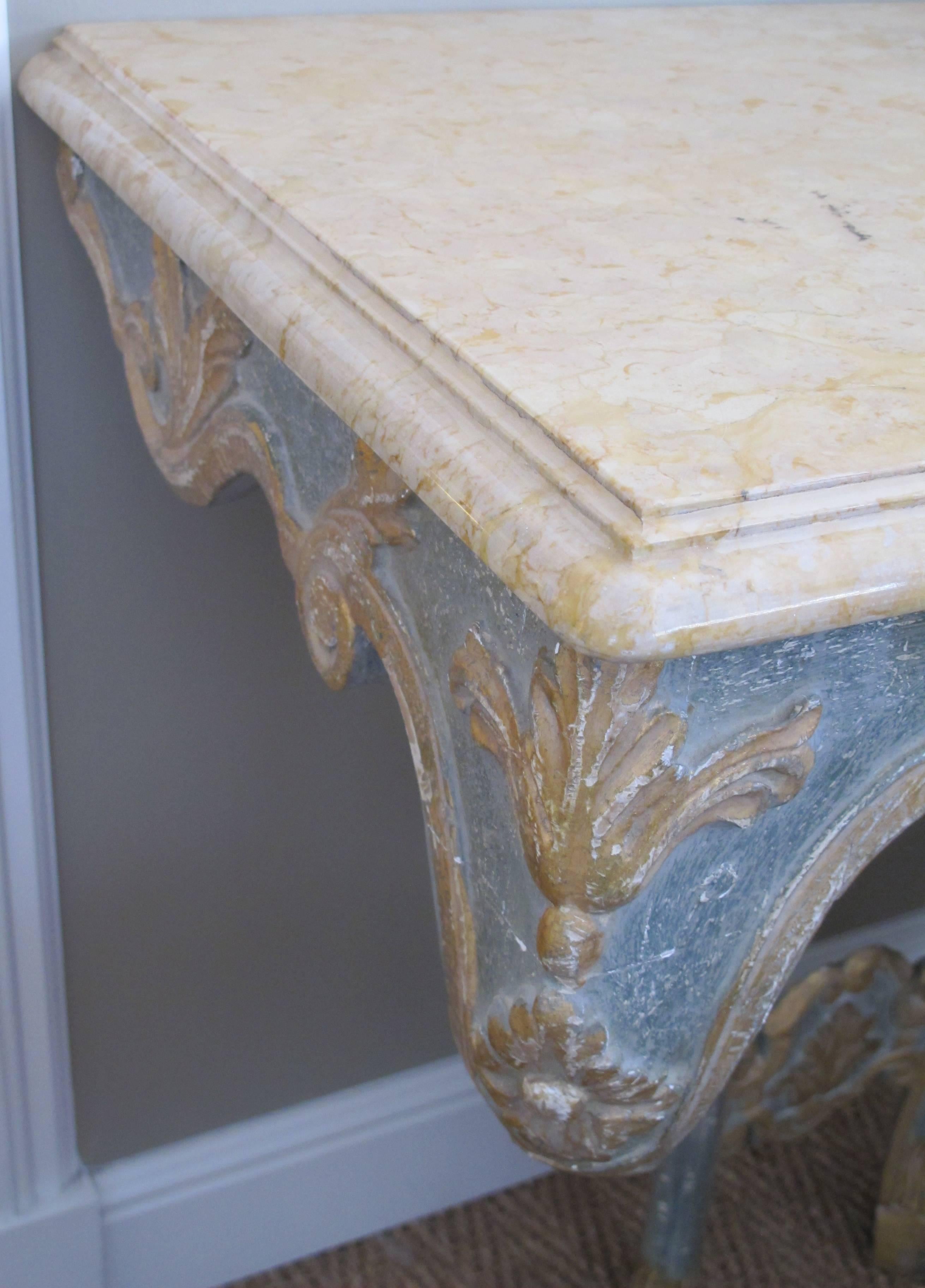 An elegant custom-made Italian Baroque style aqua and ochre painted console table with marble top; the ochre marble top resting on a well-carved aqua painted base with ochre foliate scrolls; all supported on hoof feet.