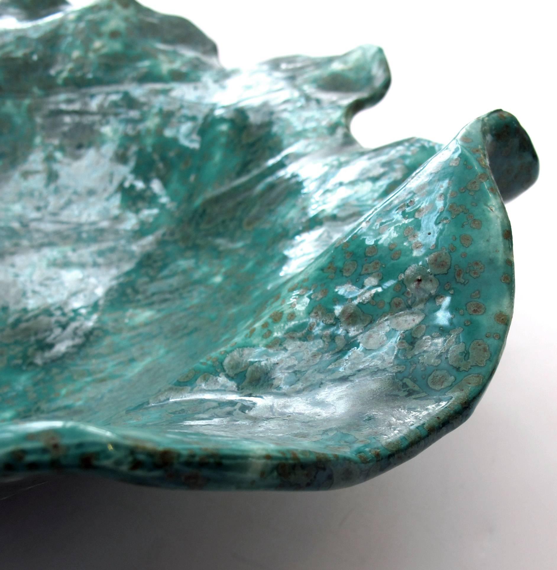 The wide bowl with undulating and scalloped edge all raised on three short feet; covered in a teal, white and olive green mottled glaze; signed 'j 01'.