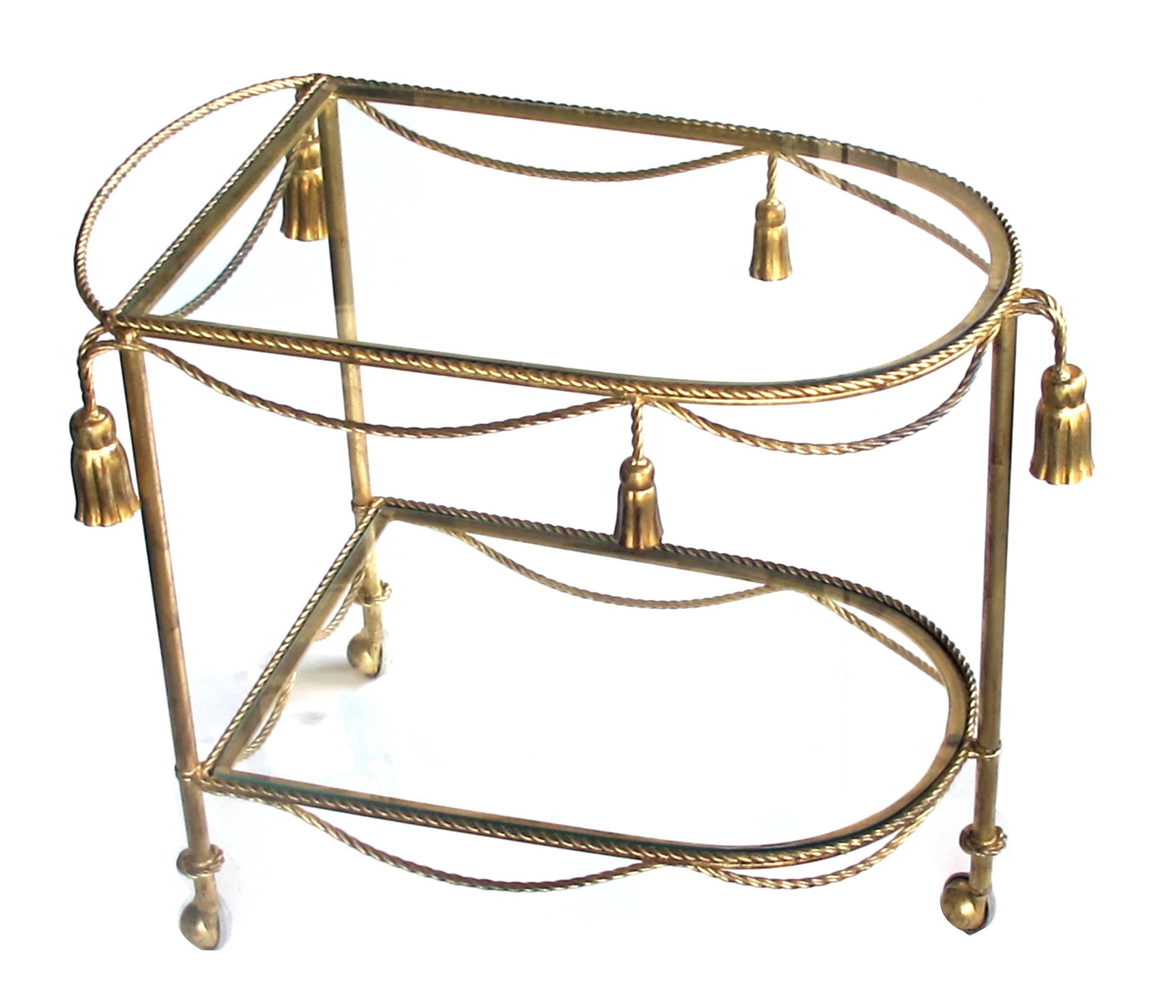 A chic pair of Italian Mid-Century Hollywood Regency gilt-tole drinks/bar carts with glass shelves; each drinks cart with rope-twist frame adorned with swags and tassels; fitted with 2 glass shelves.