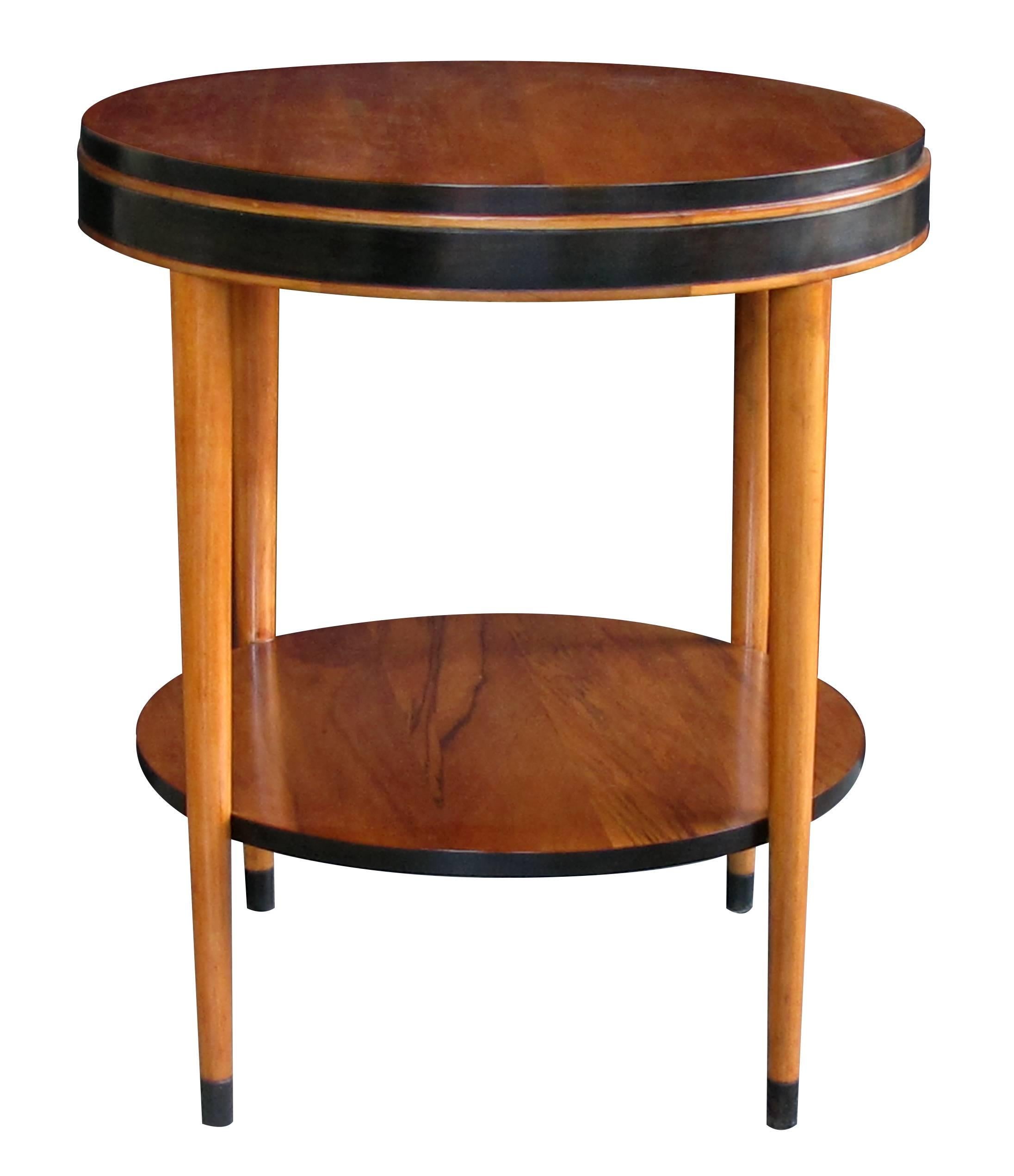 A sleek and stylish American Mid-Century Modern ash circular side table with ebonized highlights; chic and tailored in style, this circular table with stepped apron raised on tapering turned supports connected by a lower shelf.