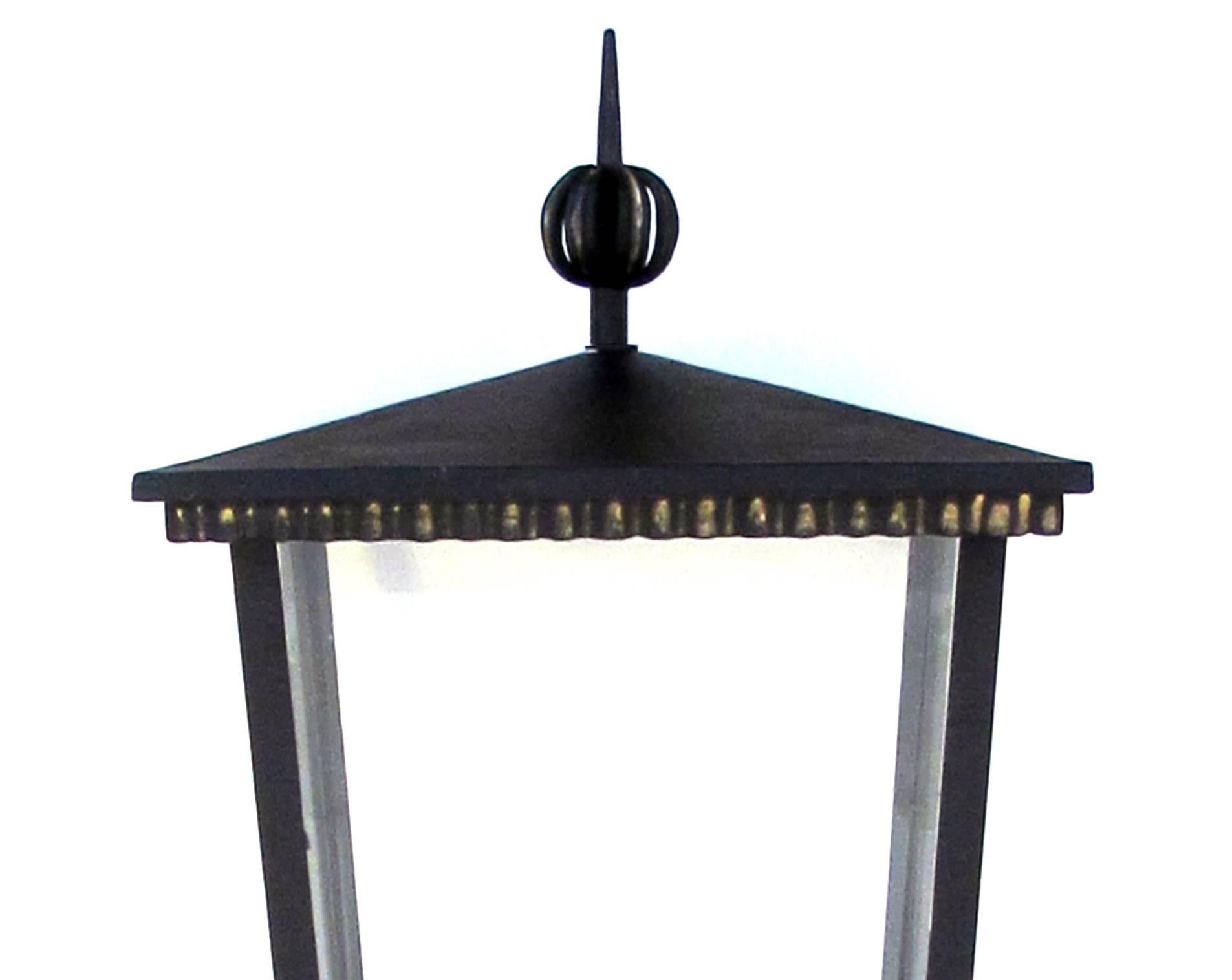 A large and sophisticated pair of French Art Deco 1930s iron and tole glazed quadrangular exterior four-light lanterns; these stunningly stylish lanterns with pitched tole hoods capped by a pointed openwork finial; above a square tapering glazed