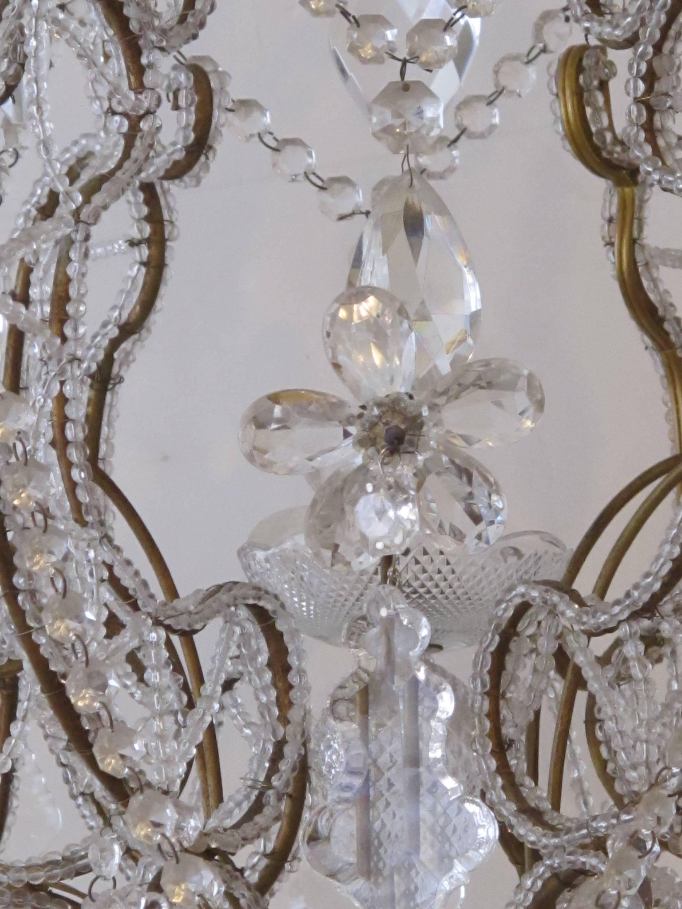 Ein glänzender und anmutiger sechsflammiger Kronleuchter im italienischen Rokokostil in Form eines Käfigs mit Perlen, Kristallanhängern, Blumen und Bändern; der zart mit Perlen besetzte Rahmen geht von sechs verschlungenen Armen aus und ist