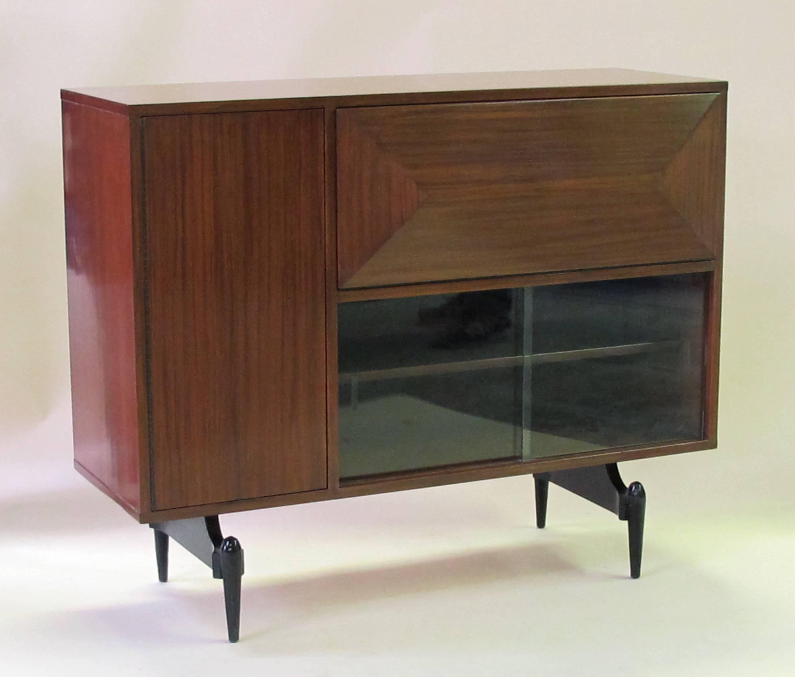 To complete that cool midcentury decor, this fine quality dry bar with hinged drop-front opening to reveal a lighted and mirrored interior fitted with caddies for glassware (original glassware included, only one glass missing); above sliding glass