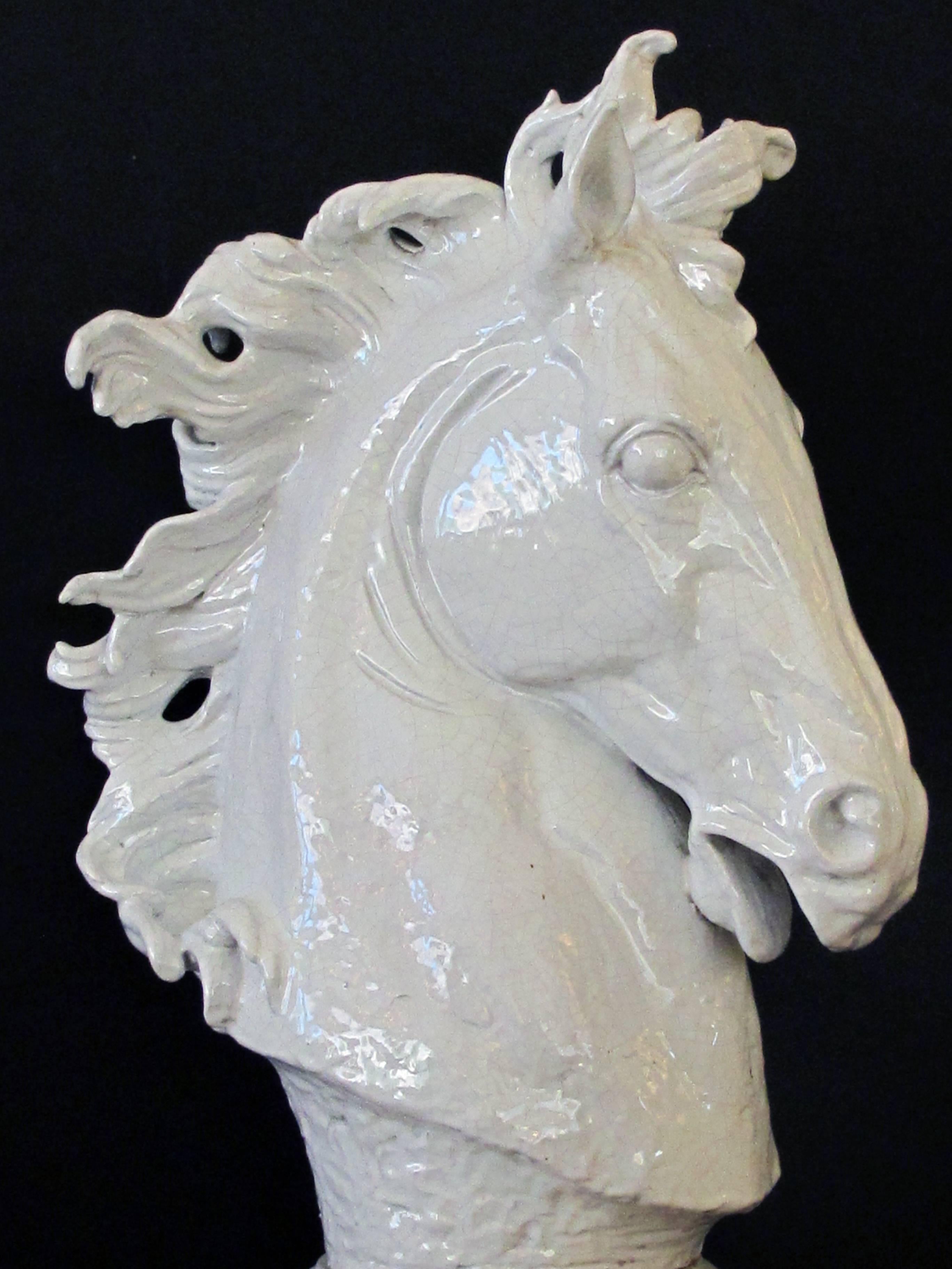 A monumental and expressive Italian Majolica midcentury white-glazed horse head; this expressive, forcefully-rendered horse head sculpture with flared nostrils and lively mane; raised on a separate base; fine overall craquelure.