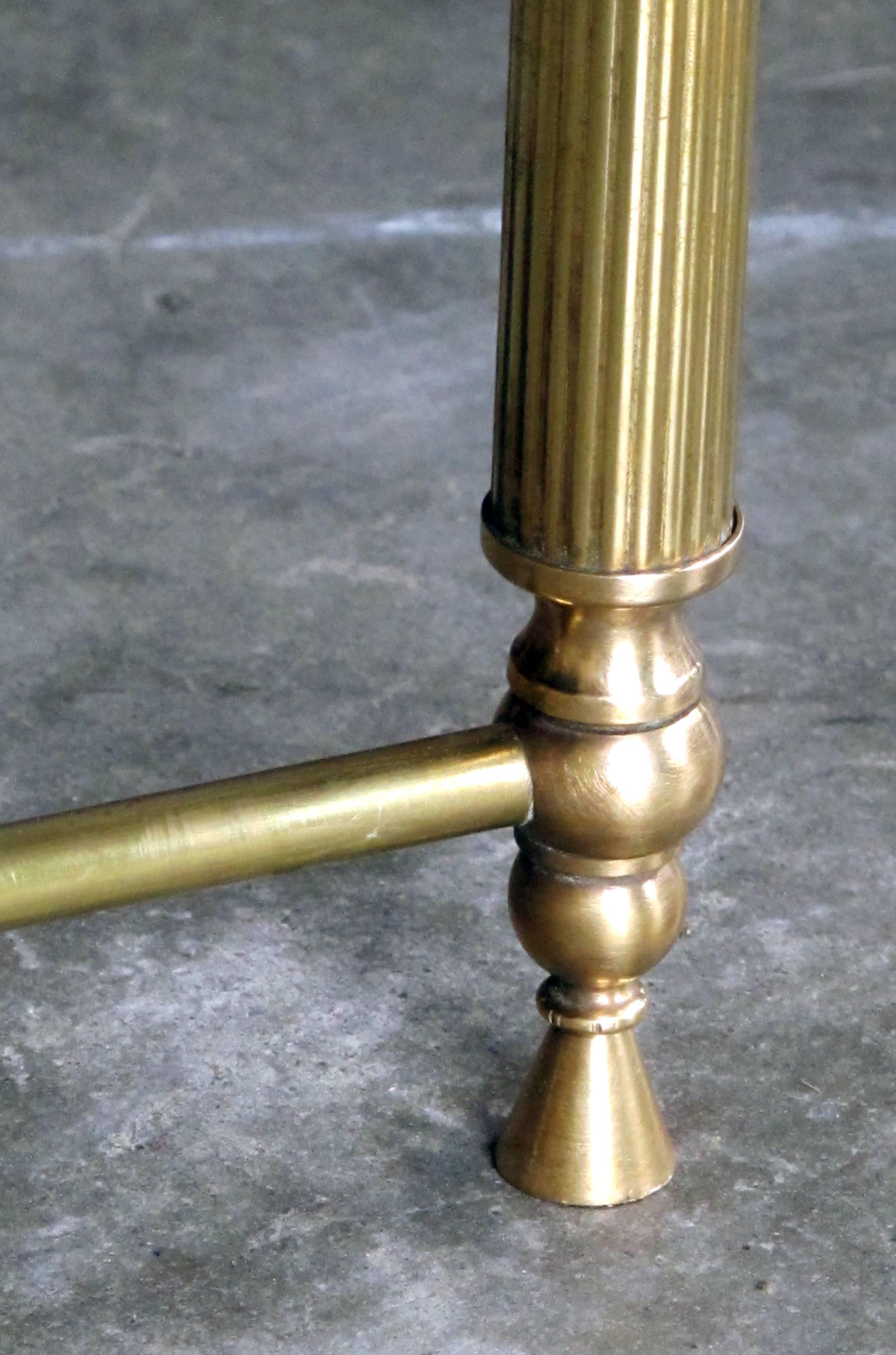 A chic French, 1940s brass rectangular coffee table with black glass top; with black glass top inset within a brass frame raised on fluted supports with stylized melon-form caps all joined by a lower x-stretcher; later glass.