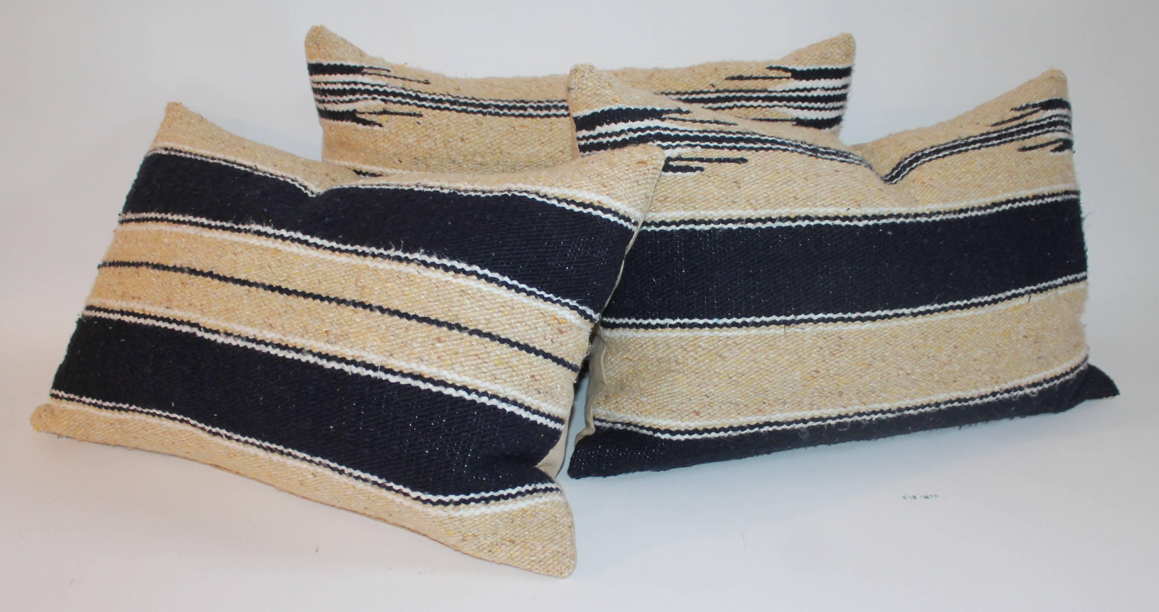 These three American Indian saddle blanket bolster pillows are in fine condition and have golden cotton linen backing. The trio are in navy blue and creamy yellow soft wool. The inserts are down and feather fill.