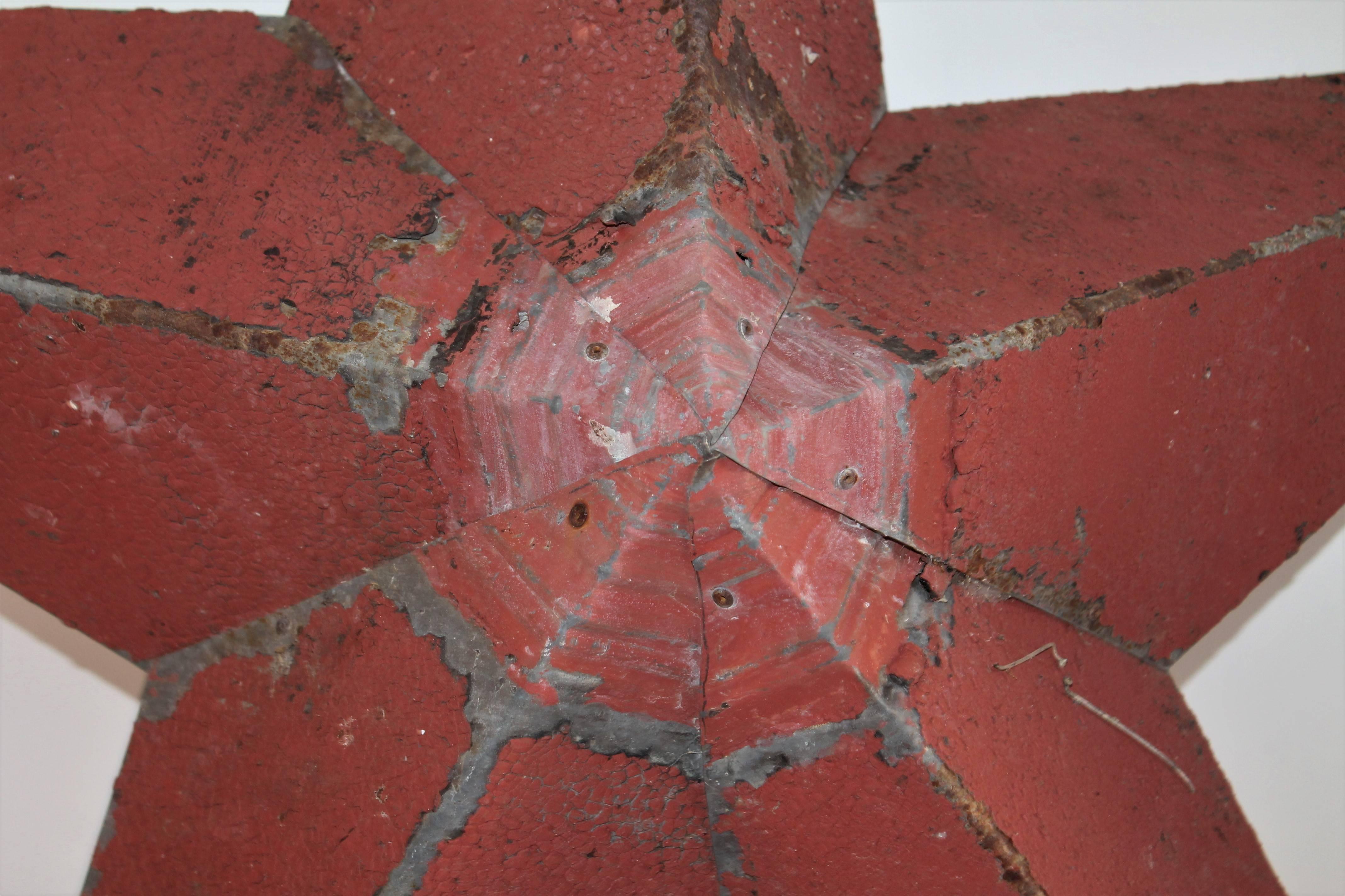 This handmade large tin star has fragments of old red crackle paint from the side of a barn in New England. The painted surface appears to be aged house or roof paint. The condition is very good with wear consistent from age and use.