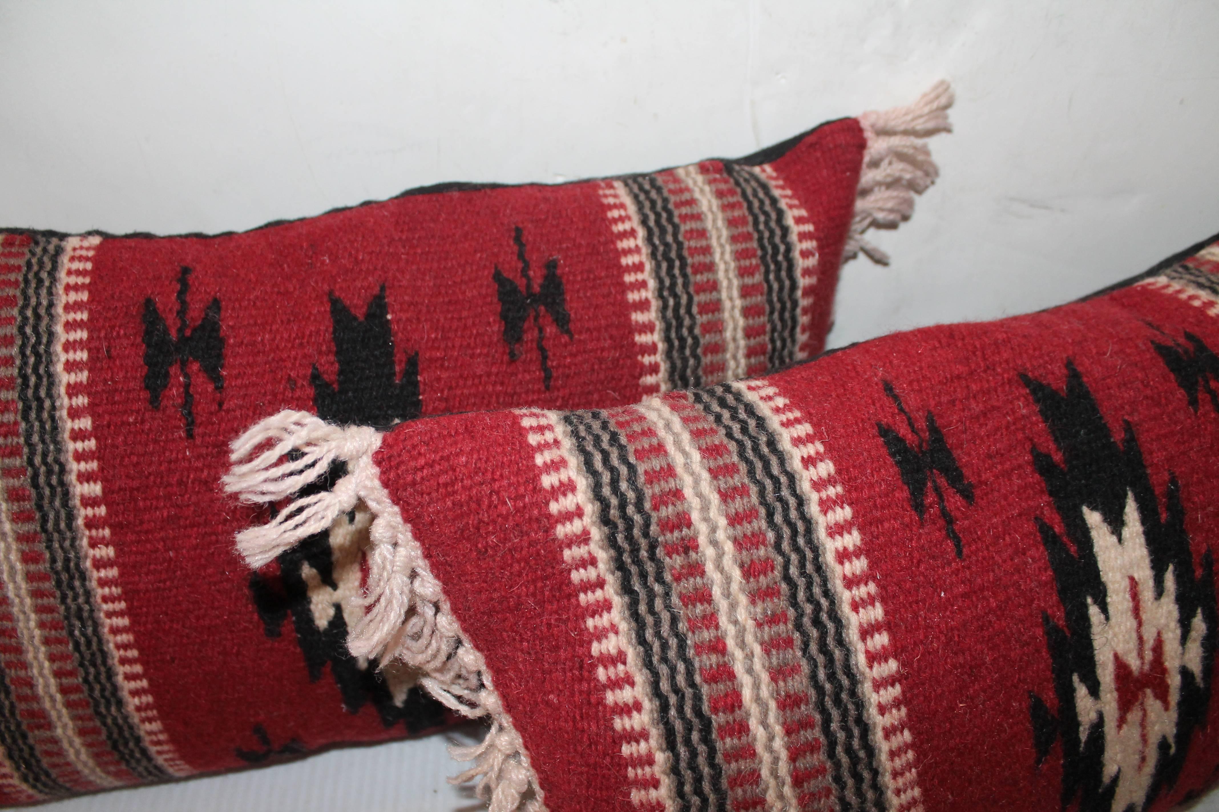 This pair of red ground hand woven pillows have cream colored fringes. Sold as a pair. The backing is in black cotton linen.