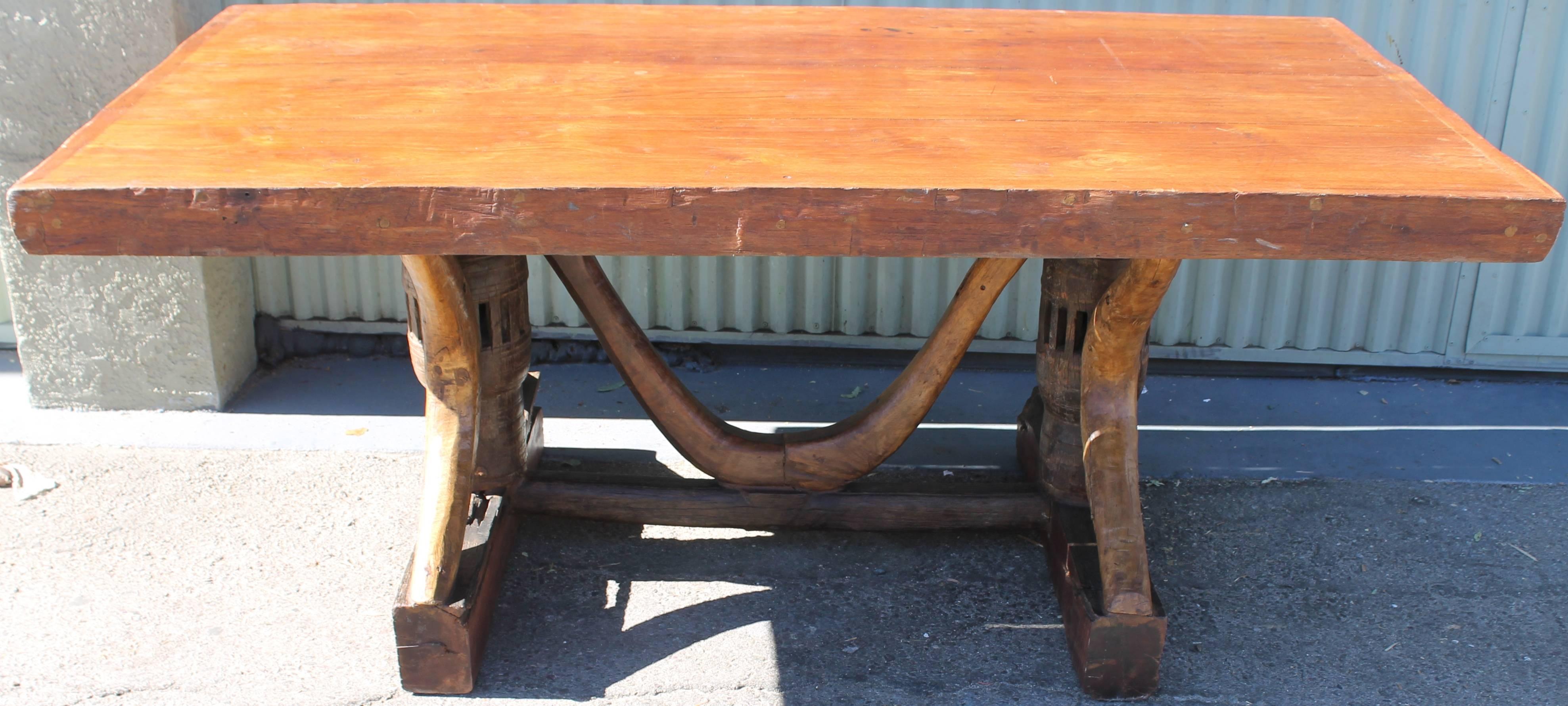 This 20th century table made from 19th century ox carts is an incredible marriage of two worlds. This all occasion table has a thick plank top with thick and strong ox cart parts and the base. This item has minor wear consistent with its age and use.