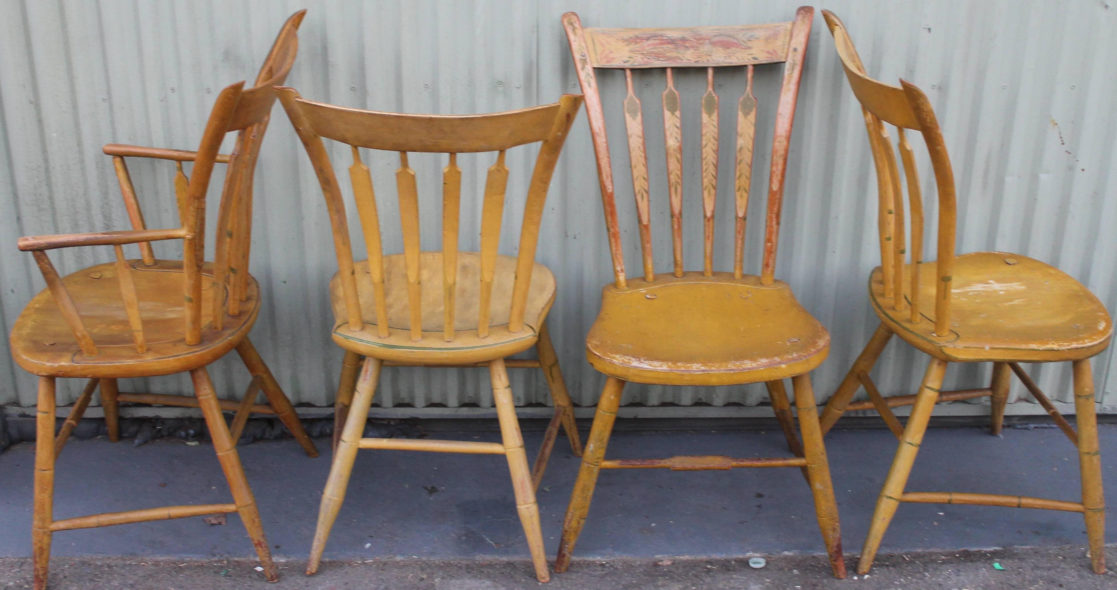This is a most unusual set of four 19th century New England decorated thumb back Windsor chairs with saddle seats. There is one fantastic arm chair and three matching dinning plank bottom chairs. These fancy paint decorated chairs have shells