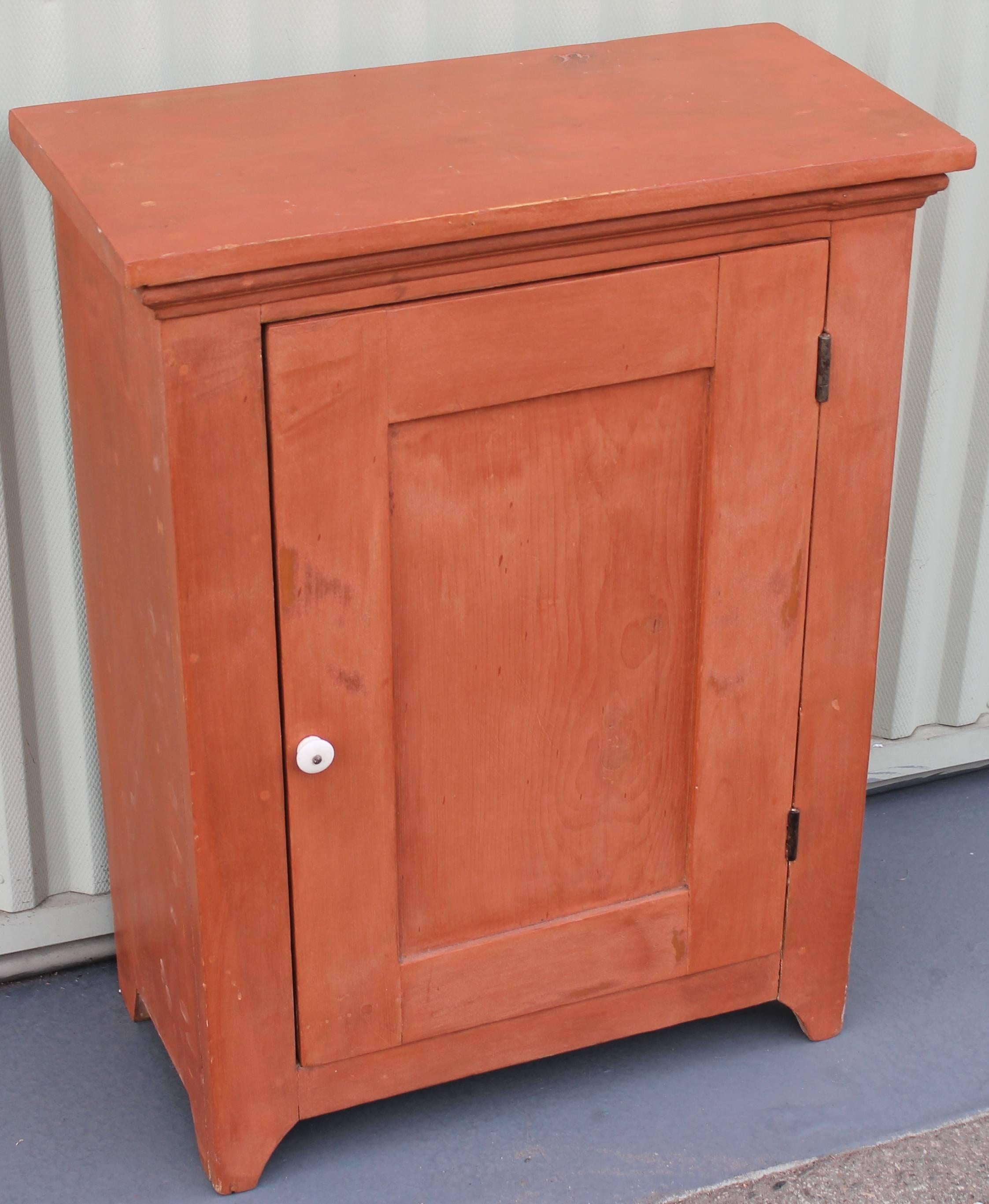This amazing one-door cupboard was found in New England and is in great as found condition. The hardware is all original and the construction is square nails and wood pegs. The interior is in a over painted white surface. This cupboard can sit on