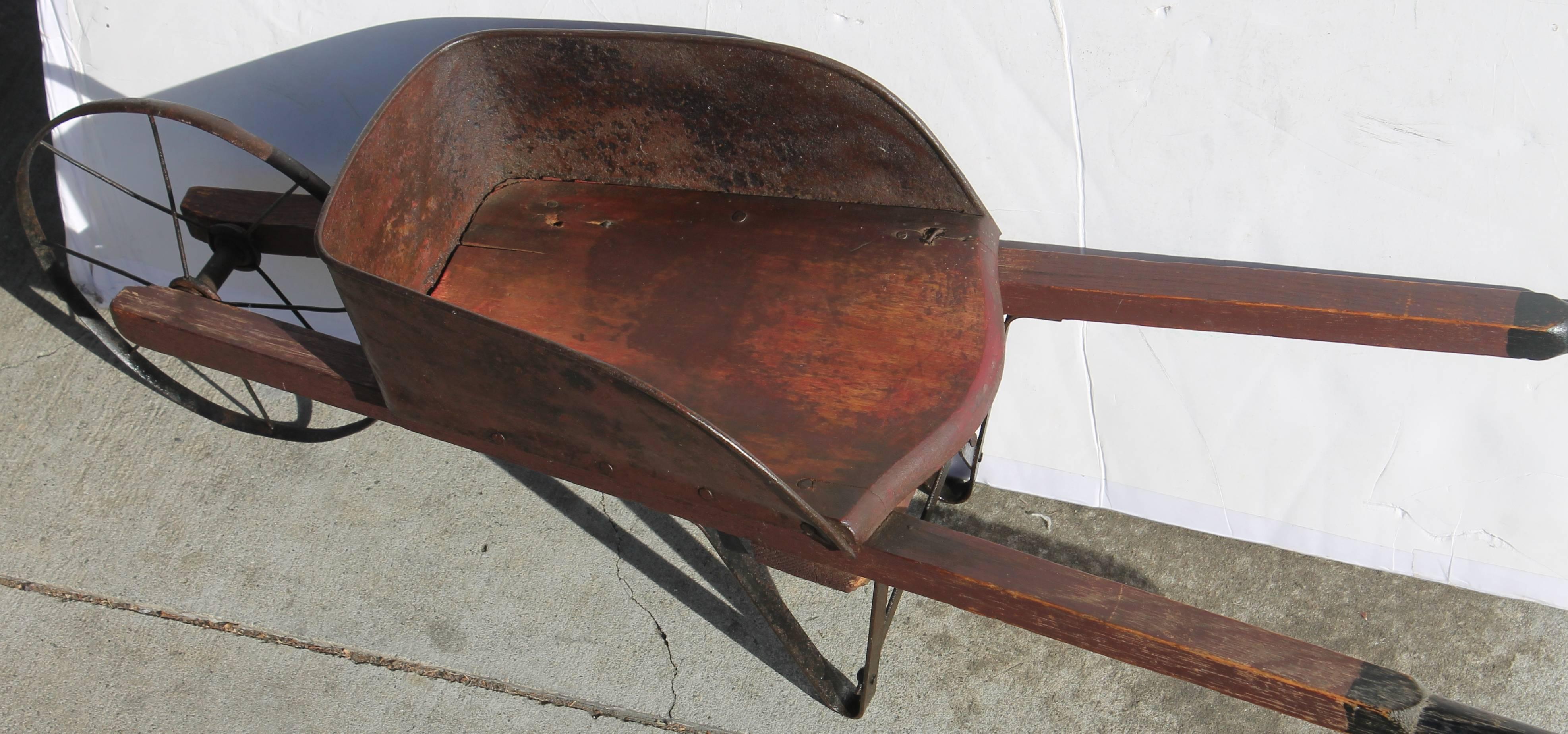 This original red painted metal children's wheel barrel has a wood insert and black and redwood painted handles. The tin and wire wheel is also original. This is a fully functional toy. Great for a teddy bear or Folk Art collection.
