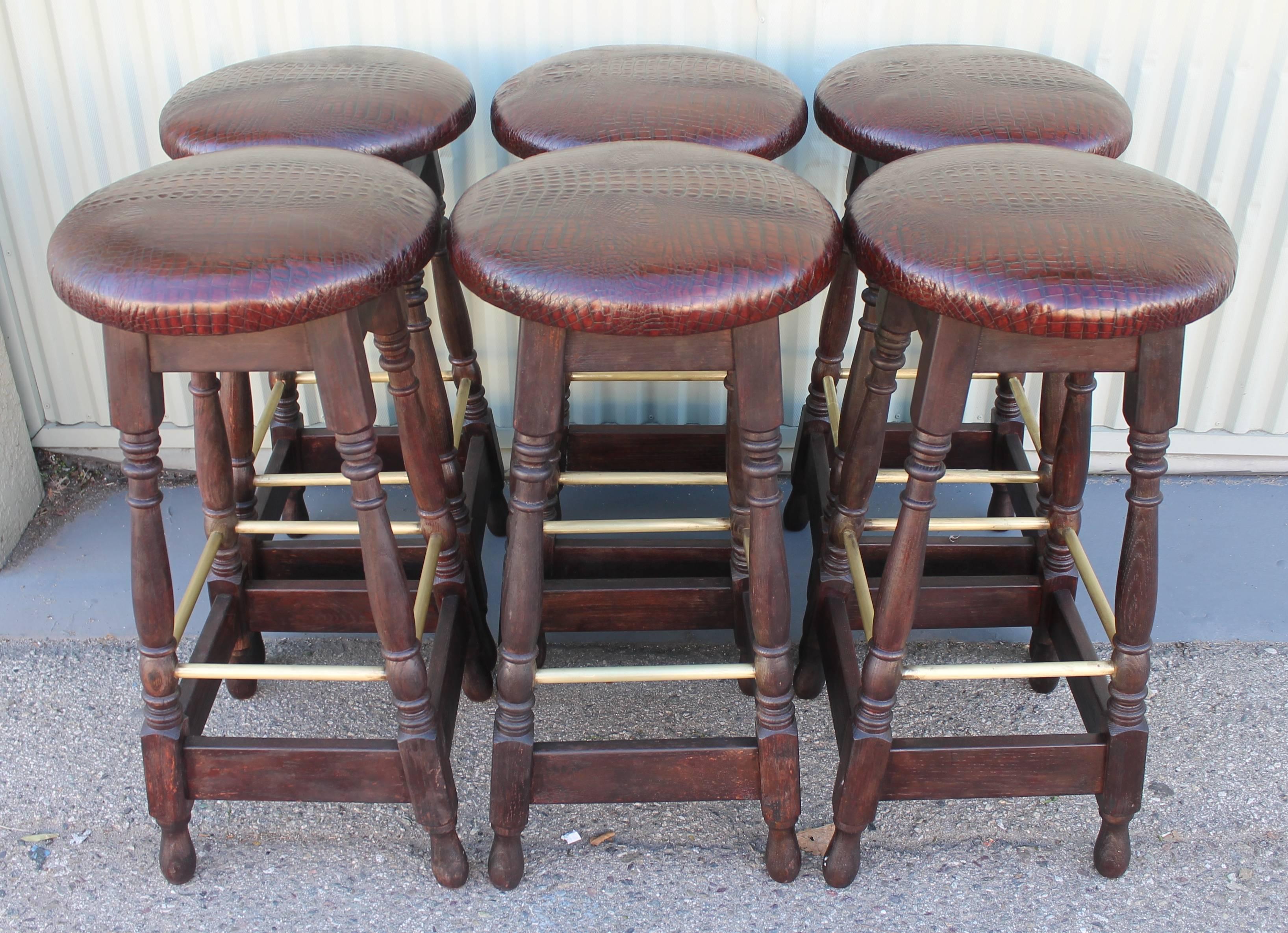 These wonderful bar stools can be sold in a pair or group of four or six. There are a total of six from the 1940s and all are in good condition. They are upholstered in a cool faux alligator leather. The brass foot rests are all original and could