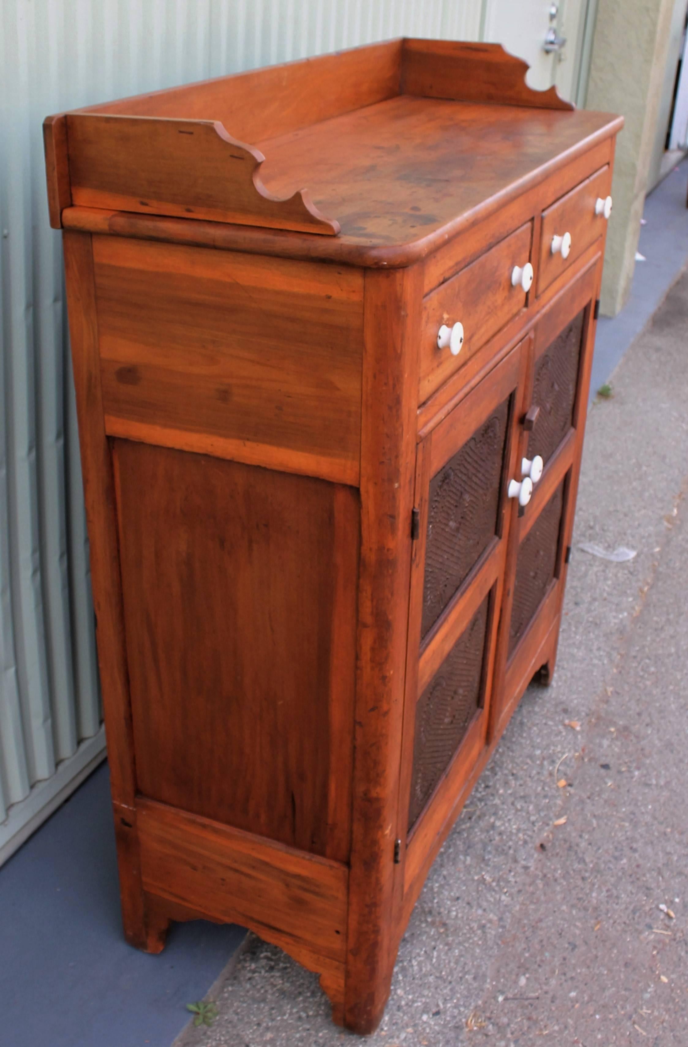 This 19th century pine two-drawer over two-door pie safe is in wonderful condition. The door panels are punched decorated tin in very good as found condition. The drawers are all dovetailed and square nailed construction with original ironstone