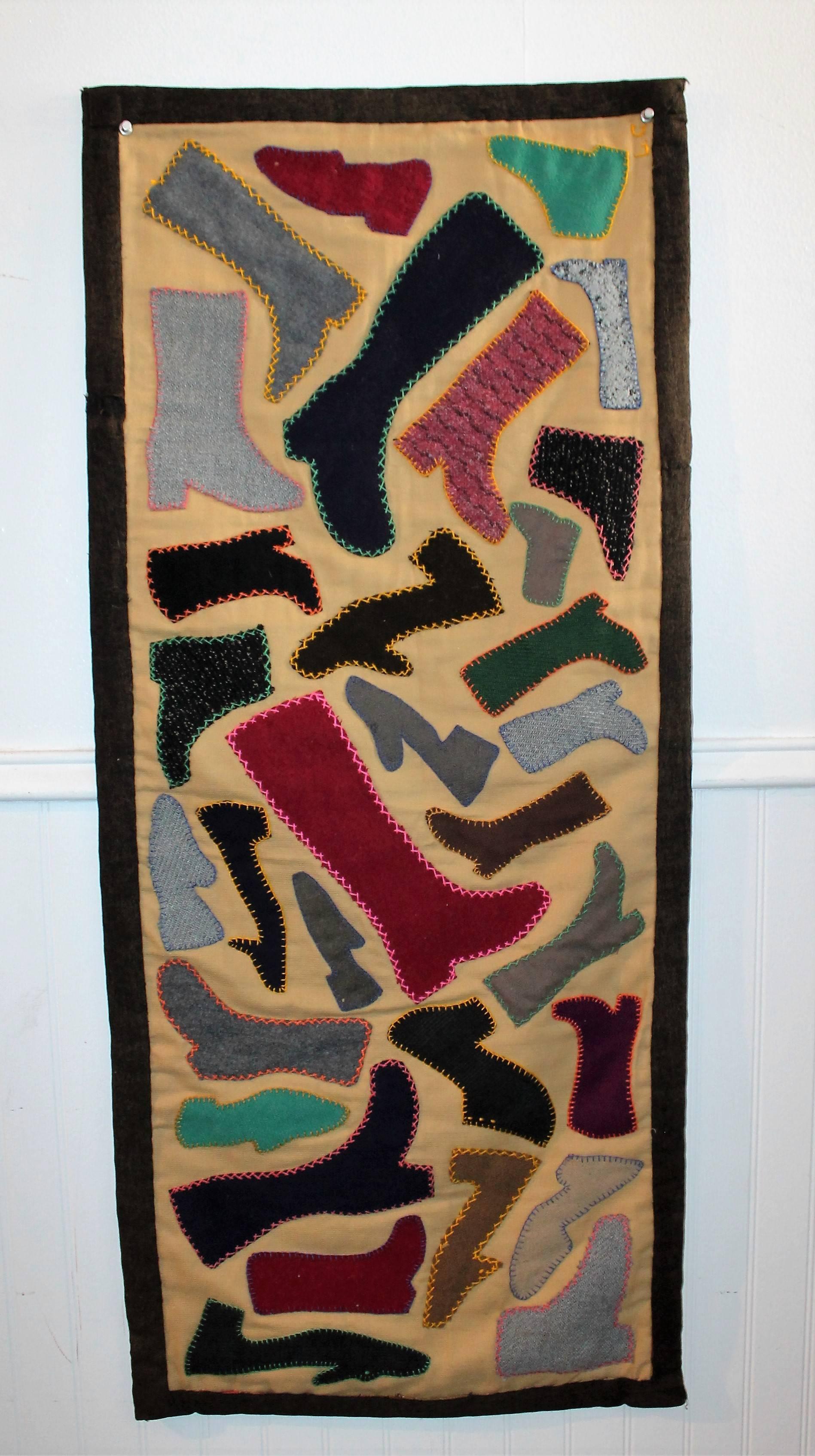 This folky pictorial handmade wool boot and shoe applique runner has the original blue ticking backing. This wonderful Folk Art textile has a velcro backing trim for hanging on a wall or framed stretcher. The binding edge is made from an old wool