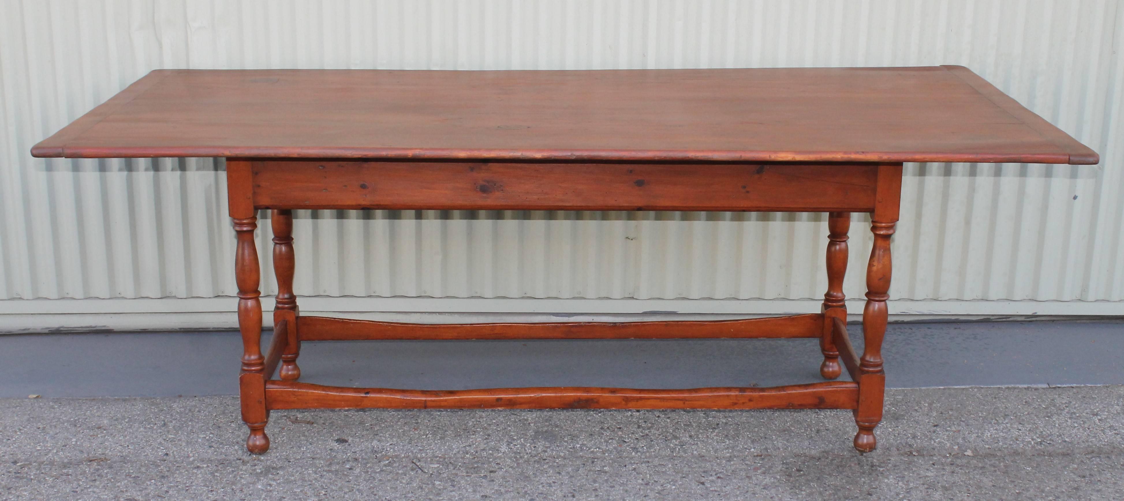 This fine country dining table was found in the state of Maine and has a wonderful aged patina. The top is a slightly painted and scrub bread board ends top. The base has a natural old stained surface and worn stretcher base. The table has wood pegs