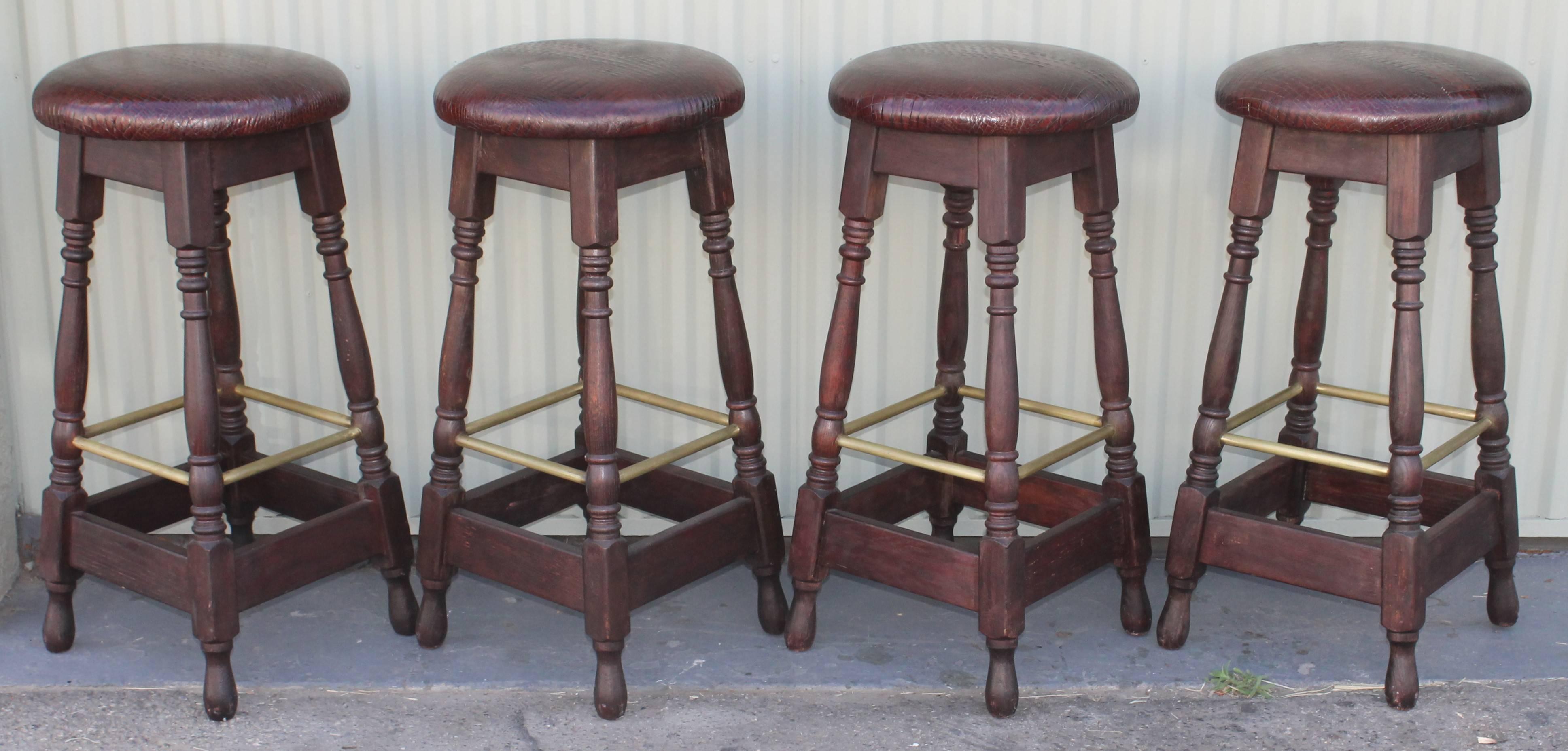 This set of four matching bar stools are in leather top seats and a turned leg base. The foot rests are in brass and are surround on all four sides. The newly done seats are in a reptile embossed texture. Fantastic condition and very comfortable.