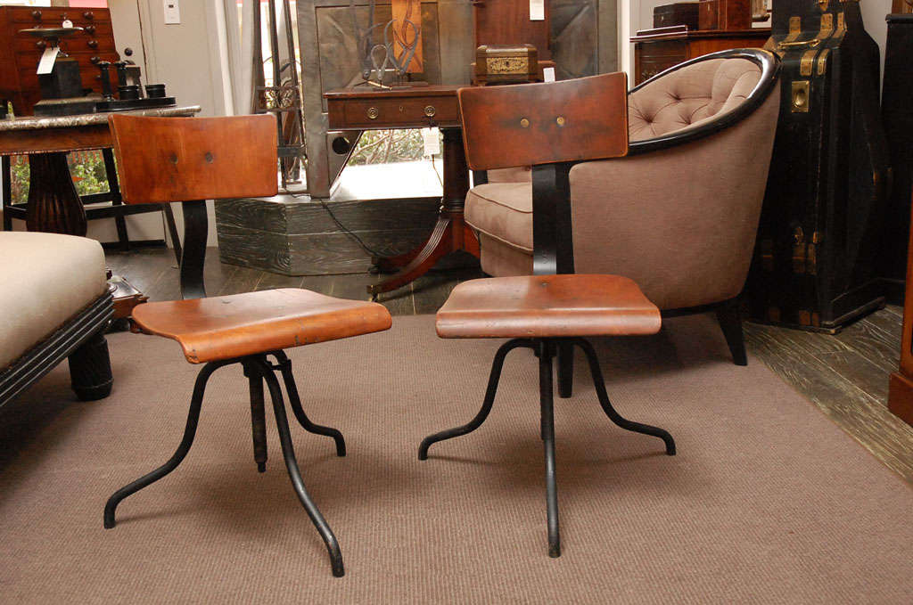Wood and iron base swivel desk chairs with a curved wood back and adjustable curved seat over splayed iron legs.