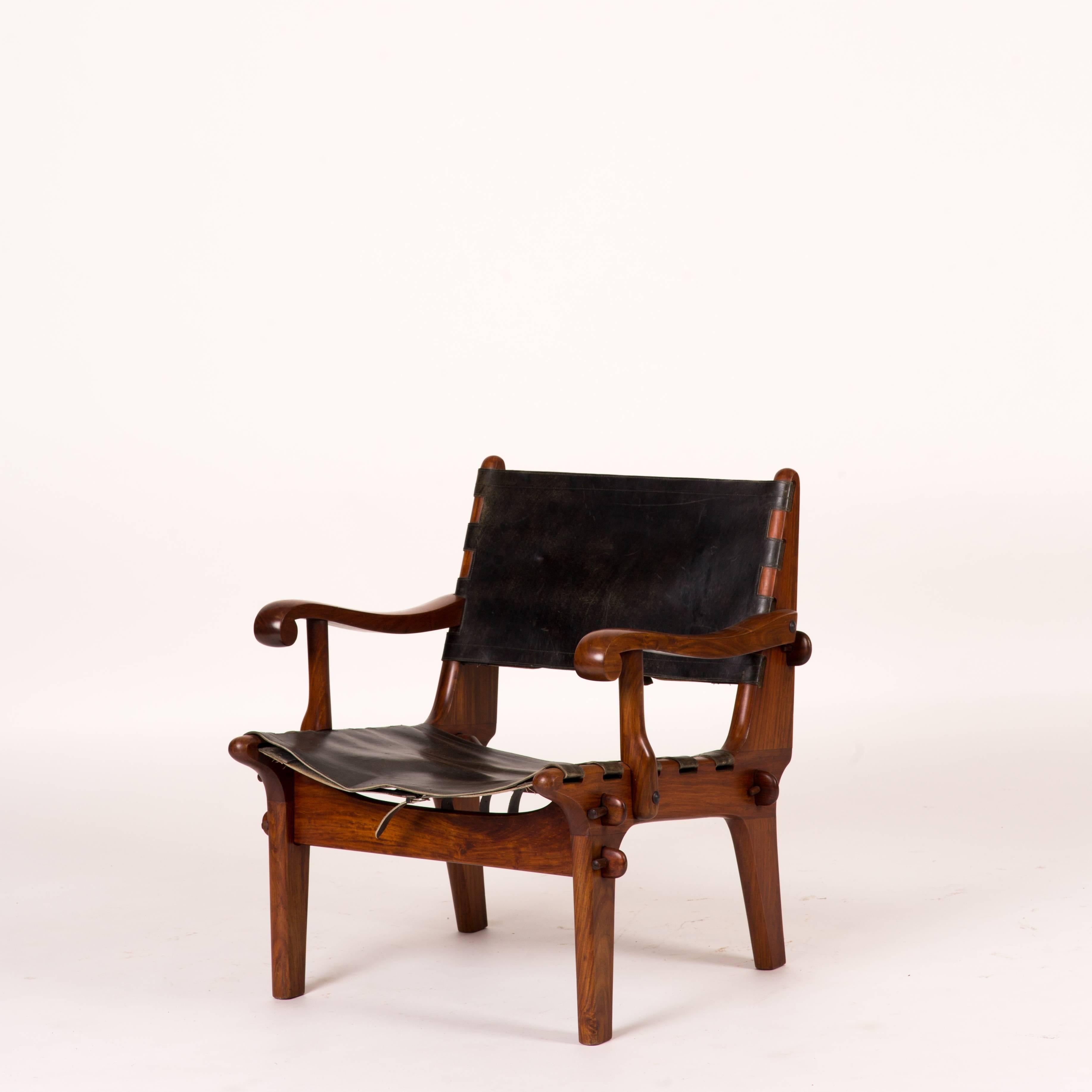 Two modernist armchairs by Angel Pazmino. These chairs feature leather slings with Aztec tooling designs often typical of Pazmino's furniture. Both chairs come with a footstool of the same design.