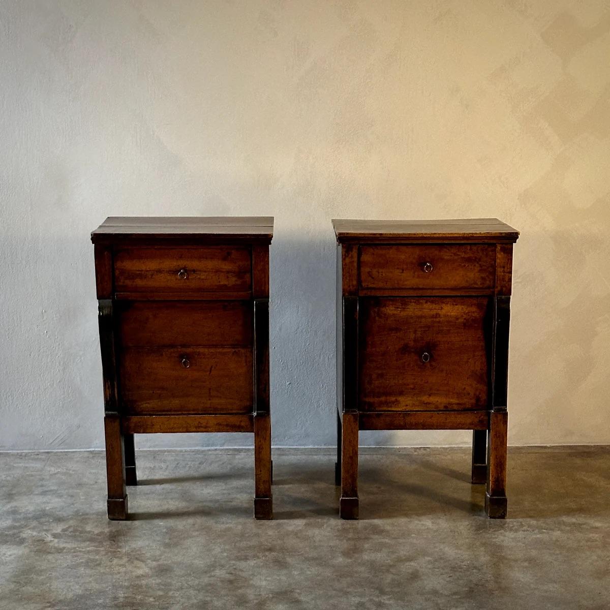 Paire de tables de chevet de style Empire en noyer, originaires de l'Italie du début du XIXe siècle. Chaque table présente un design épuré avec deux tiroirs, affichant des lignes simples et épurées typiques de l'esthétique Empire. La finition chaude