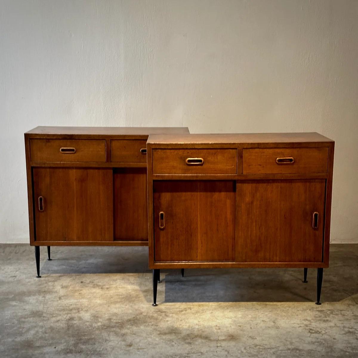 Pair of Italian 1960s walnut wood sideboards featuring sleek, hardware-free drawers and spacious cupboards below. These mid-century chests of drawers are supported by thin spindle legs, embodying the era's minimalist elegance. The rich walnut finish