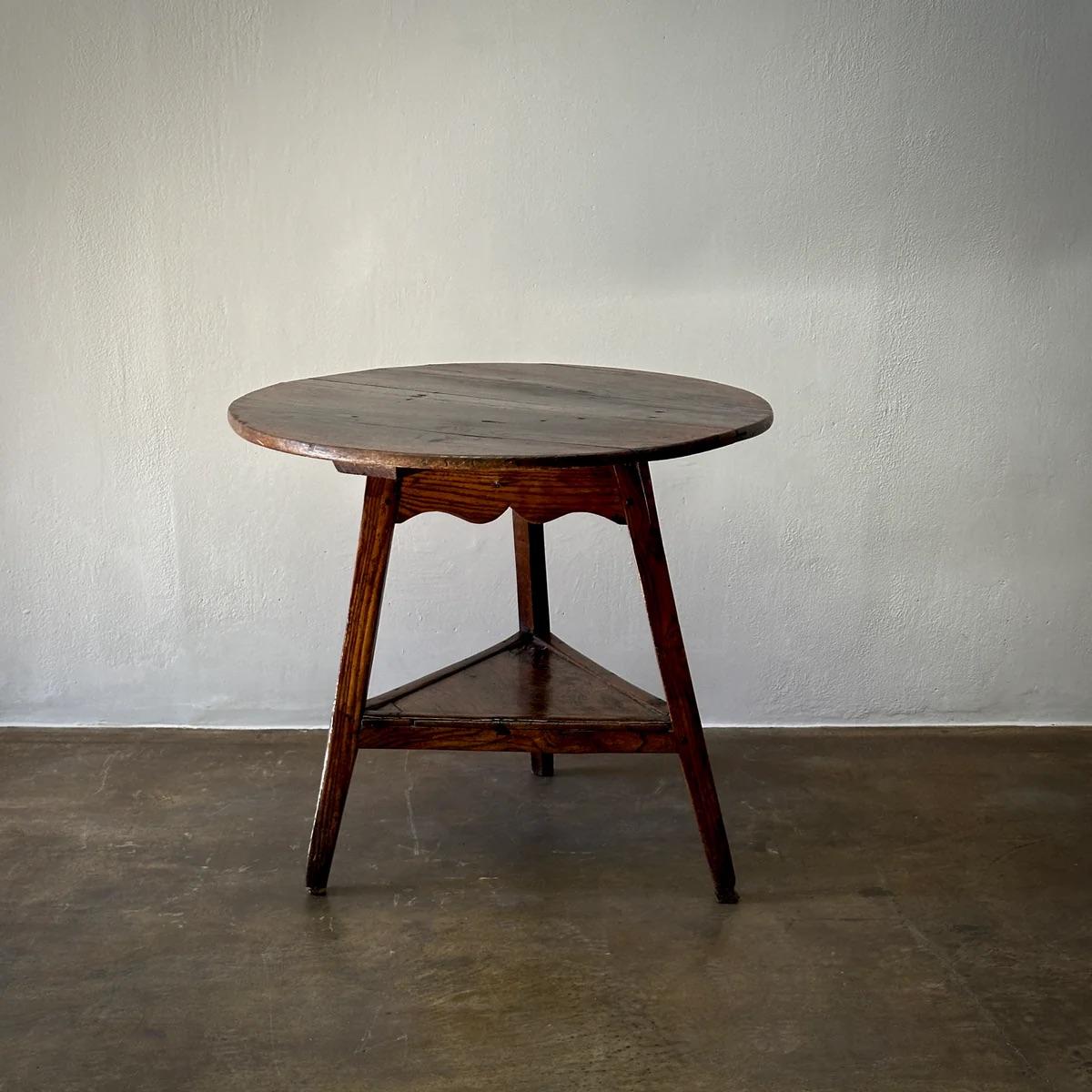 Cette table de cricket anglaise du XIXe siècle présente un plateau rond en bois et une base tripode caractéristique avec une étagère inférieure triangulaire. Le design présente des lignes simples et traditionnelles, conférant à la pièce une