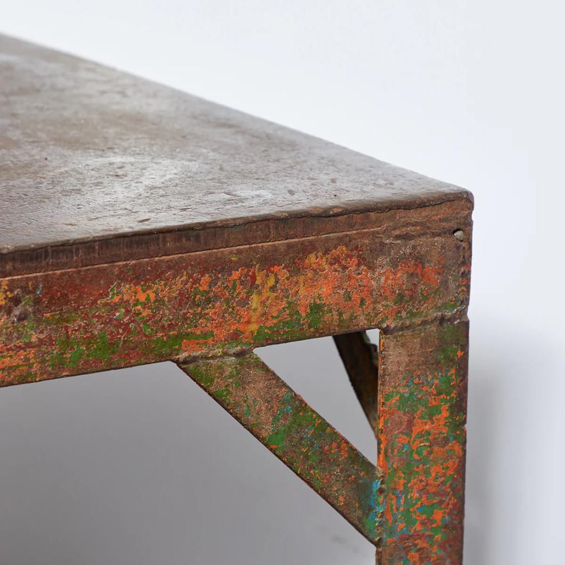 This industrial iron table features an incredible patina with traces of original paint in a spectrum of hues. The design maintains a robust simplicity with its straight-lined legs and elongated rectangular top, making it a versatile choice for use