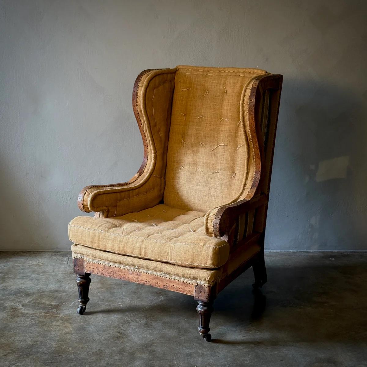Sillón inglés de proporciones y presencia sorprendentes, que muestra su tapicería original de crin de caballo y arpillera bajo un armazón desnudo. El respaldo alto, las alas esculturales y la generosa profundidad reflejan la artesanía de la época, a