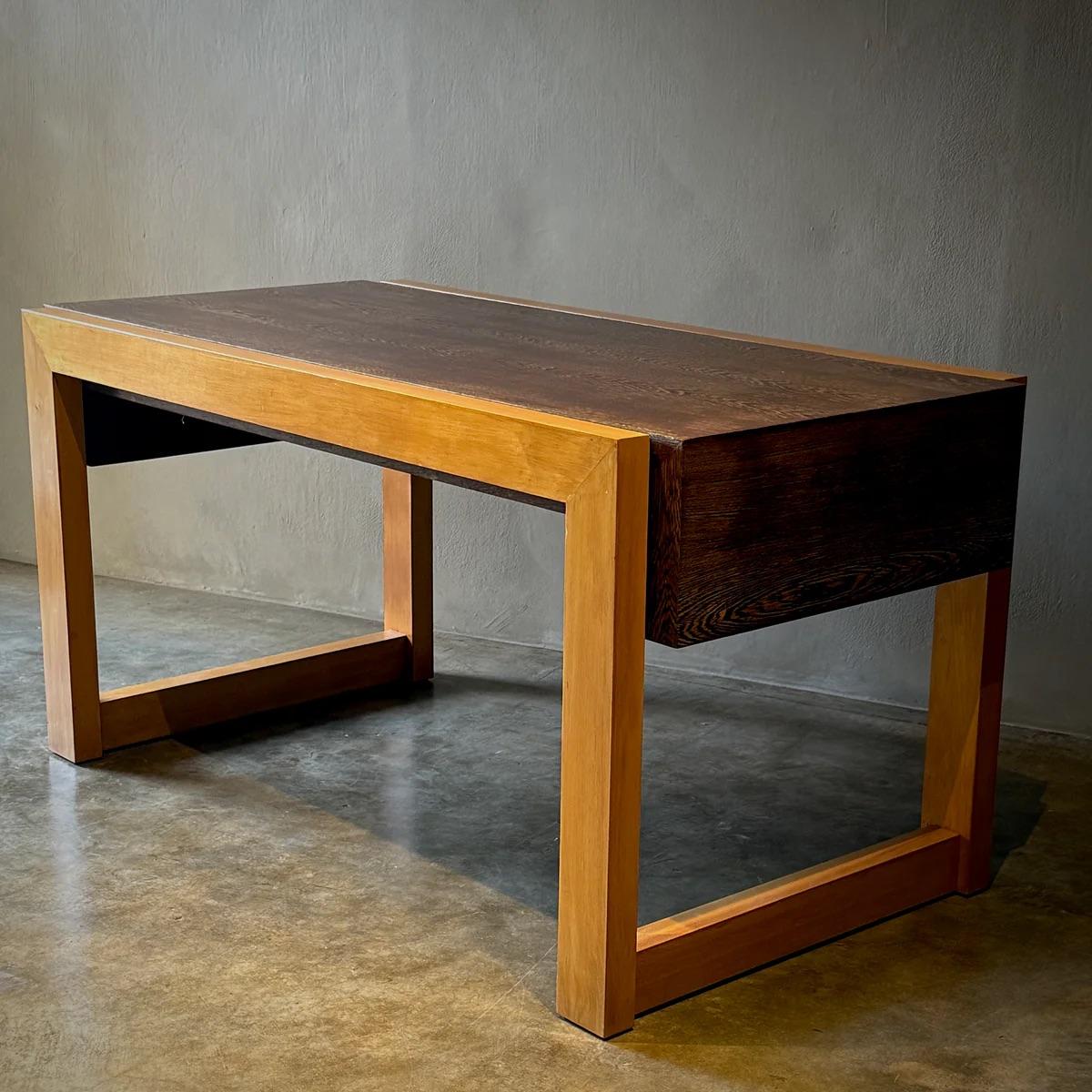 This minimalist writing table features a striking wenge wood top that contrasts beautifully with its lighter wooden frame. The design is sleek and contemporary, with clean lines and a sturdy structure that prioritizes both style and function. The
