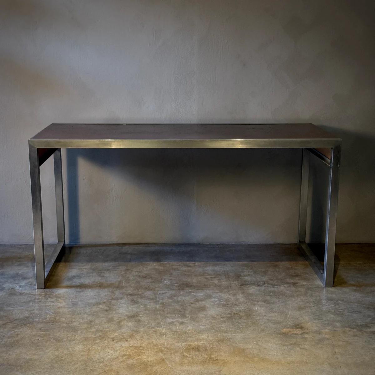 Cette table d'écriture française allie la précision industrielle à une palette de matériaux raffinés. La structure métallique élégante constitue une base solide et moderniste, tandis que le plateau en cuir texturé apporte chaleur et profondeur. Avec