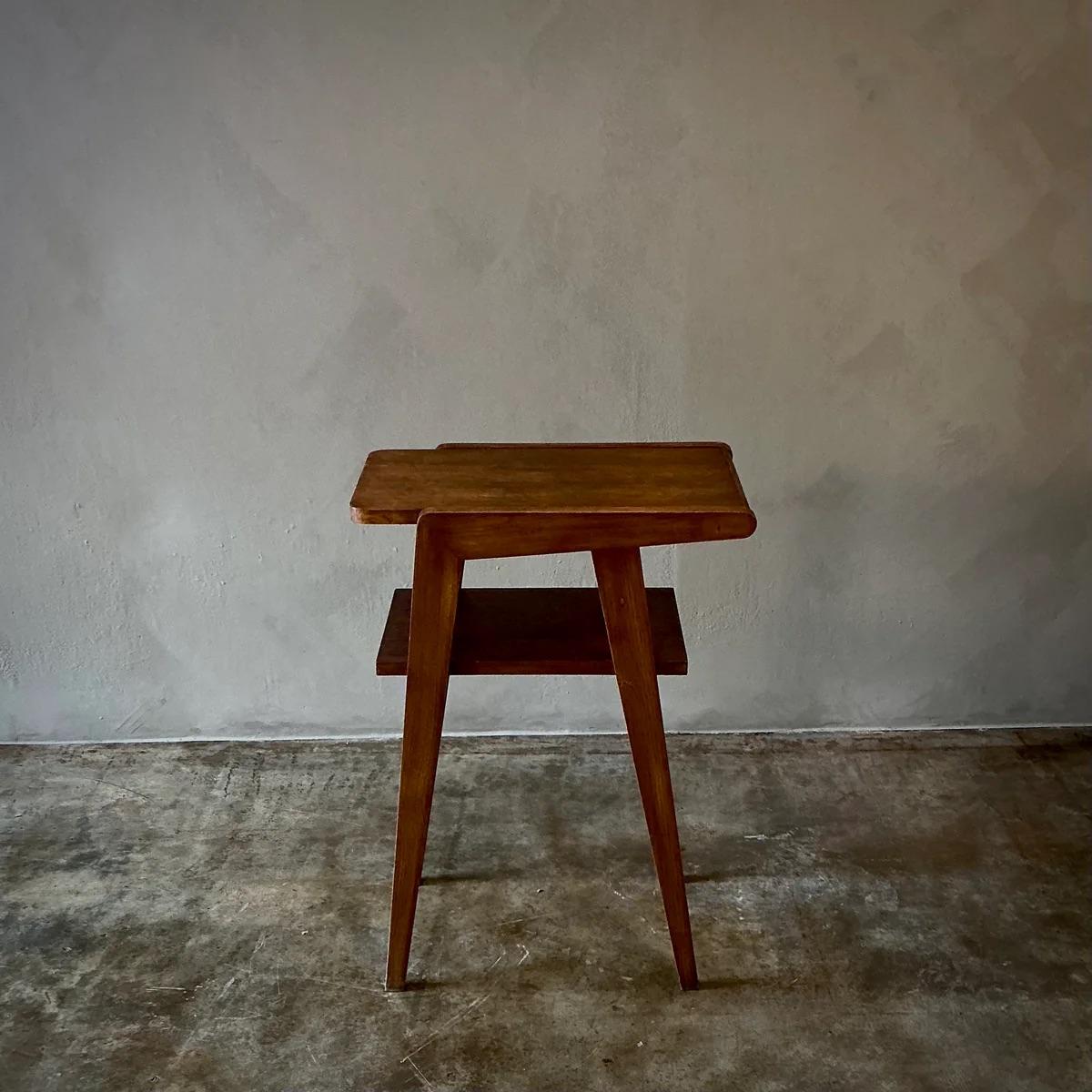 This modernist side table, crafted from rich, dark wood, exemplifies the simplicity and functional aesthetic of early mid-century design. The table features a unique cutout on the tabletop and is supported by slender, tapering legs that give it an