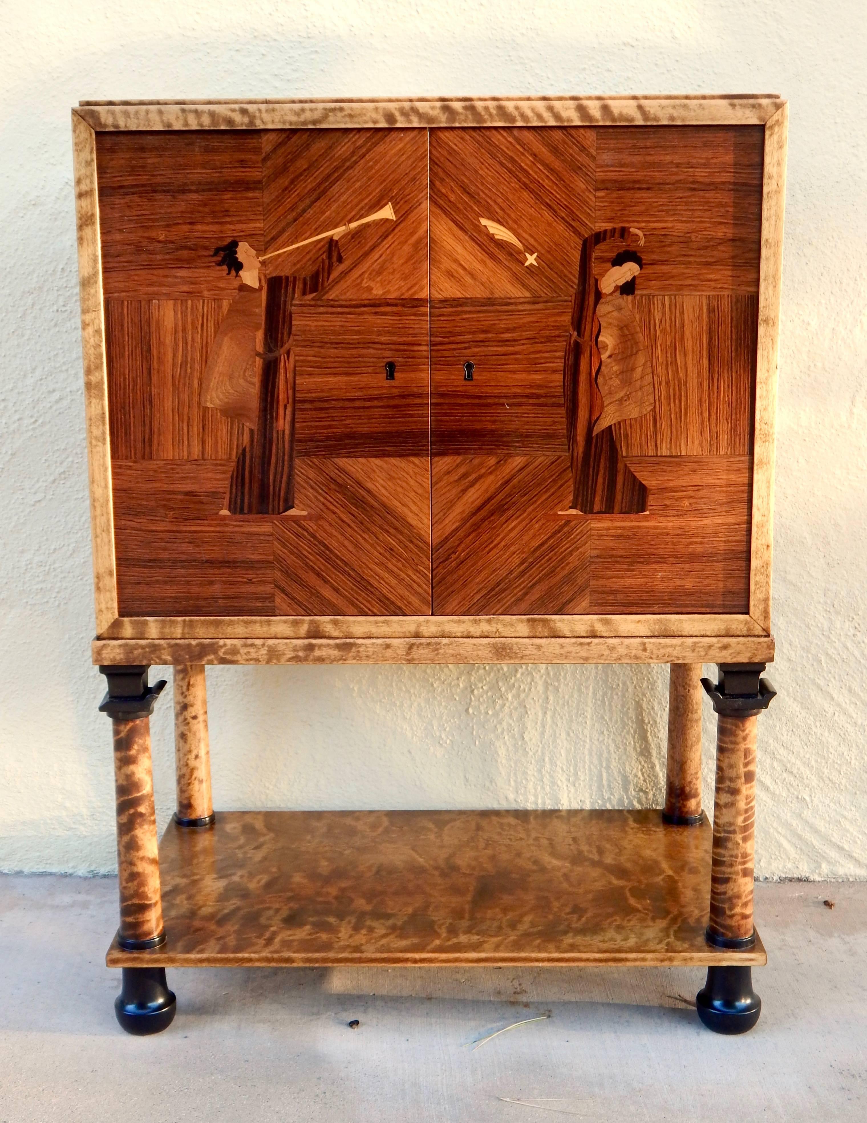 Swedish Art Deco inlaid bar cabinet by Mjölby Intarsia, Mjölby, Sweden, circa 1930. Rendered in golden flame birchwood with ebonized detailing on leg tip and column. Inlaid doors in rosewood, Carpathian elm, ebony and Karelian birch. This cabinet is