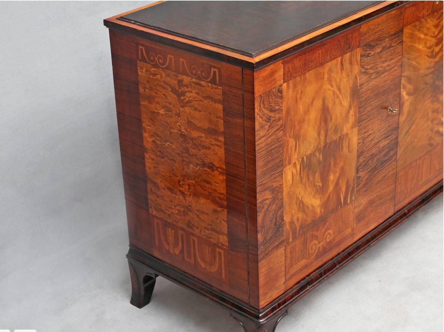Swedish Art Deco inlaid sideboard cabinet by Erik Chambert, circa 1930. Rendered in golden flame birch and rosewood with mixed wood neo-classically themed inlay. Ebonized details on base and moldings. Interior consists of two small drawers, A