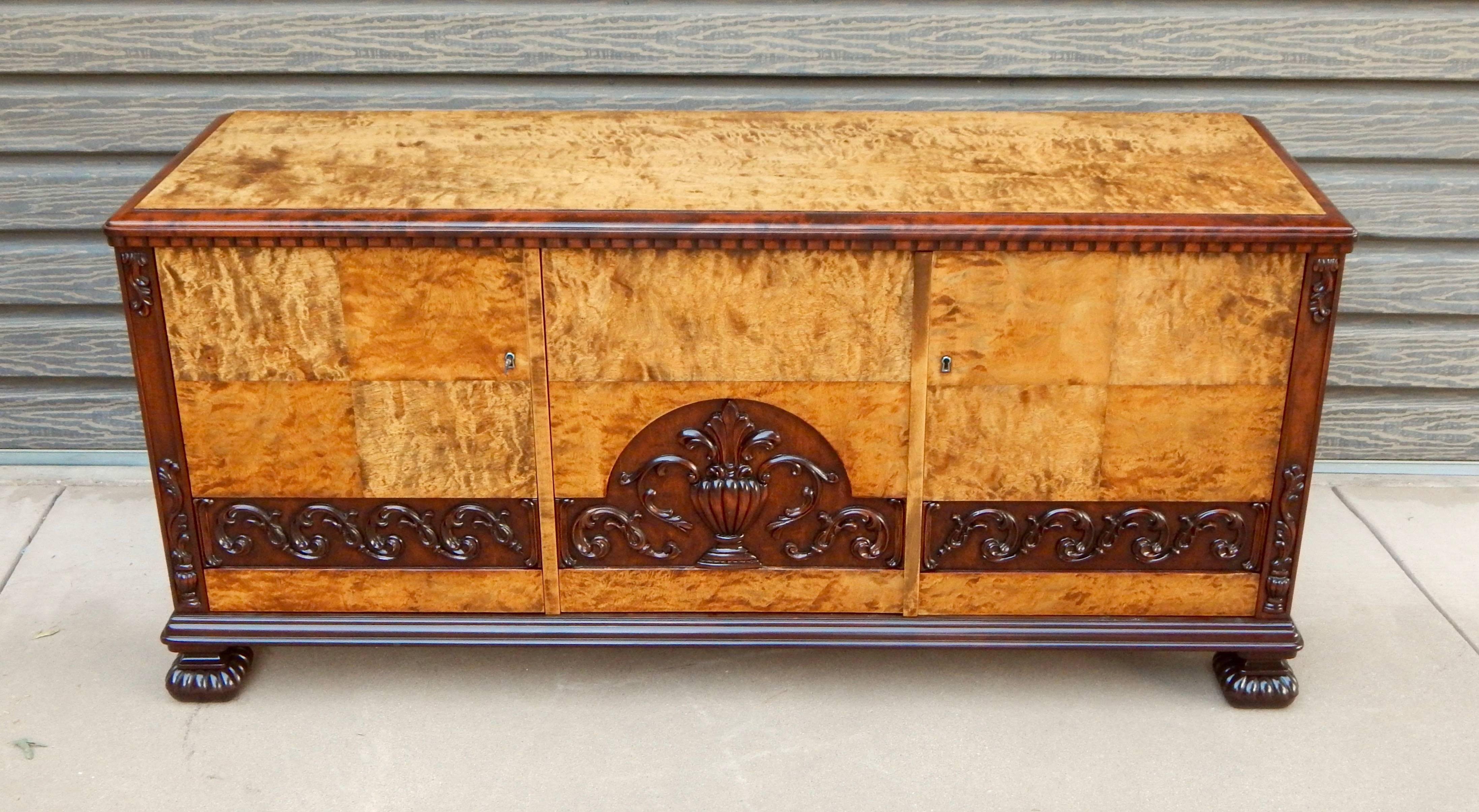 Swedish Art Deco neo-classically inspired sideboard cabinet rendered in bookmatched, highly figured golden flame birchwood. Neo-classically inspired high relief carving and detailing in stained birch. Made in Sweden in the 1920s. Beautifully