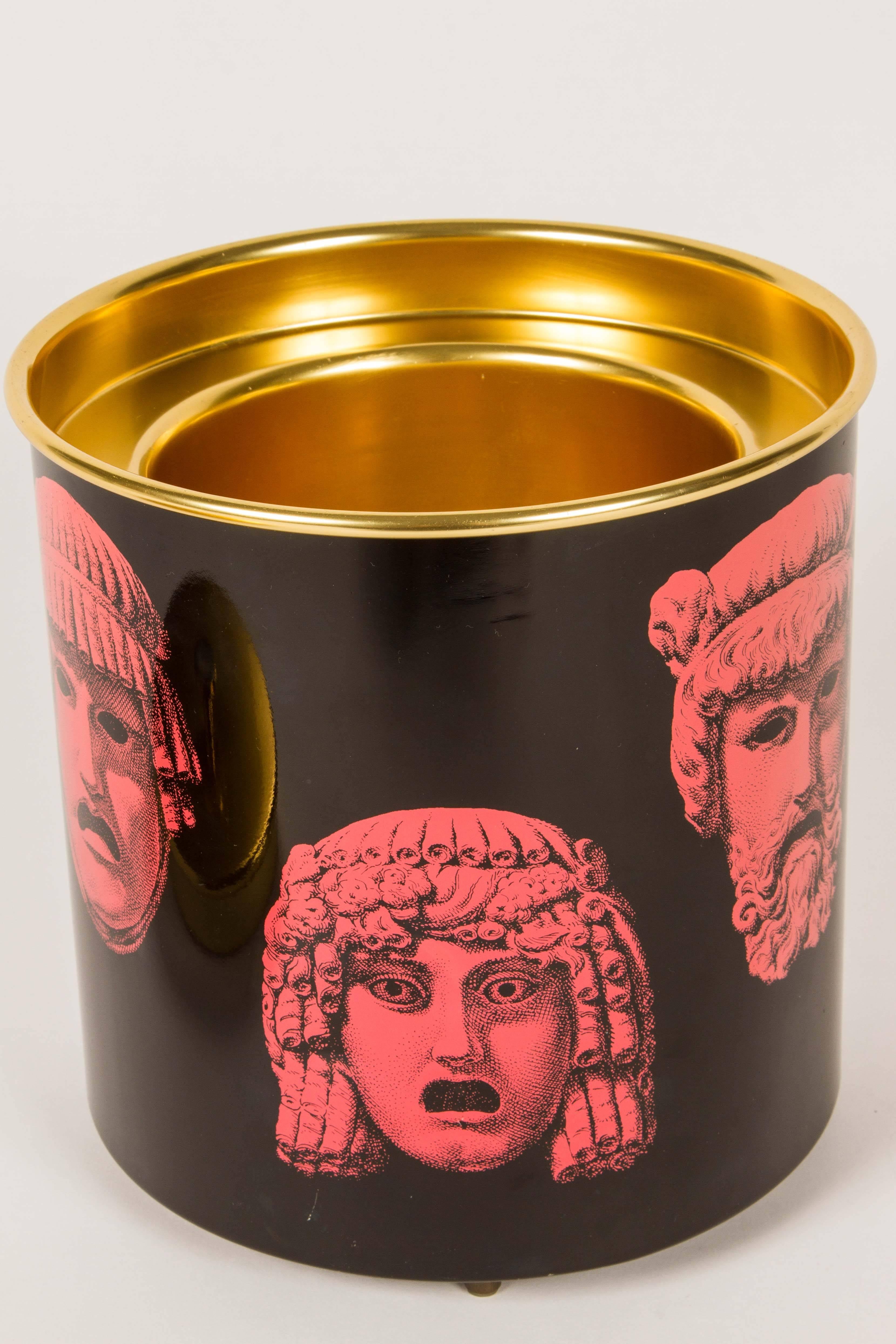 This is a wonderful period ice bucket in a striking combination of black, red and anodized gold lid. The bucket features various Greek or Roman masks. There are the remnants of an original inventory sticker on the side of the bucket as seen in image