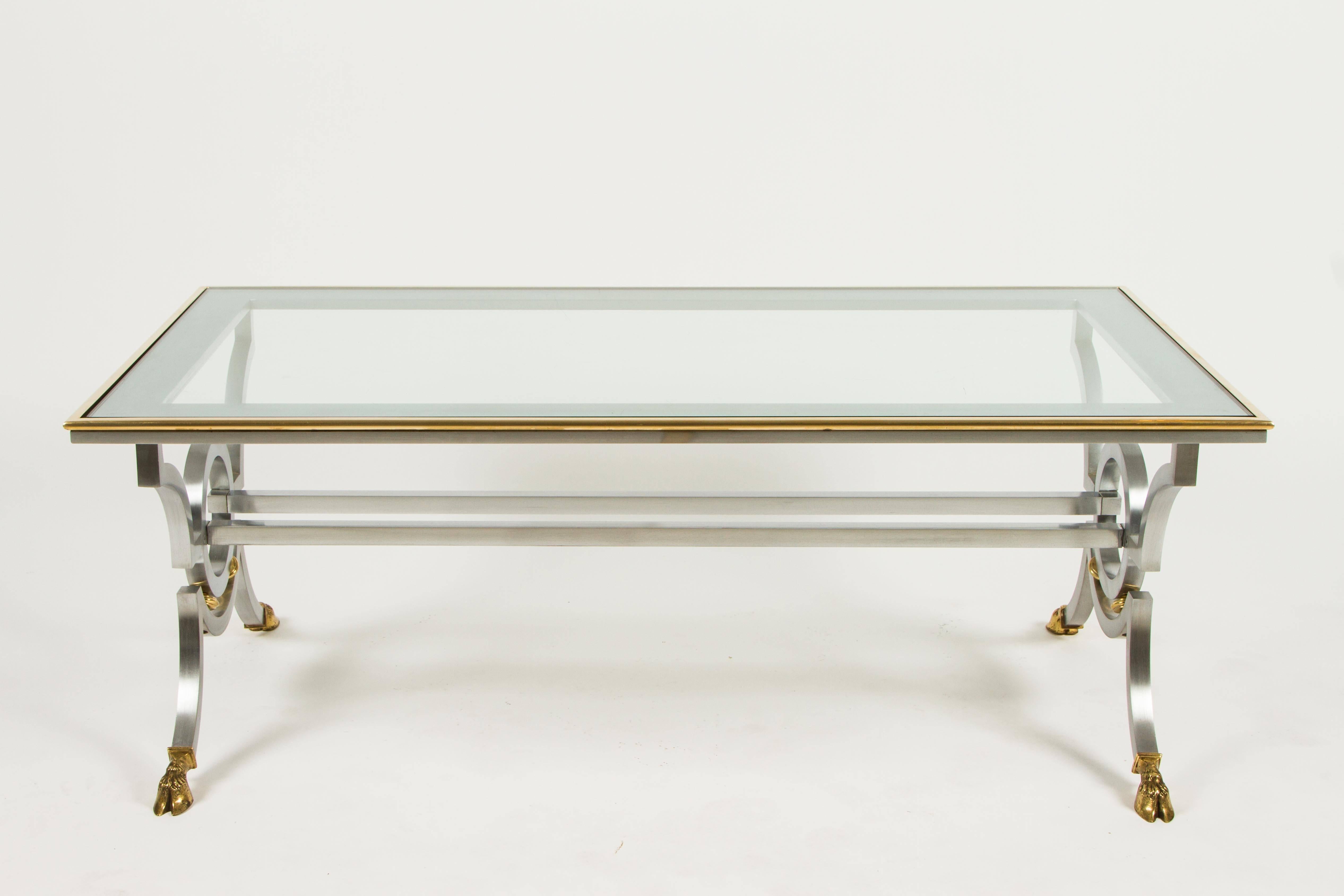 This stylish table features a brushed steel frame accented by brass including hove feet. The top is surrounded by a band of brass. Reminiscent of works by Maison Jansen this table is very chic.