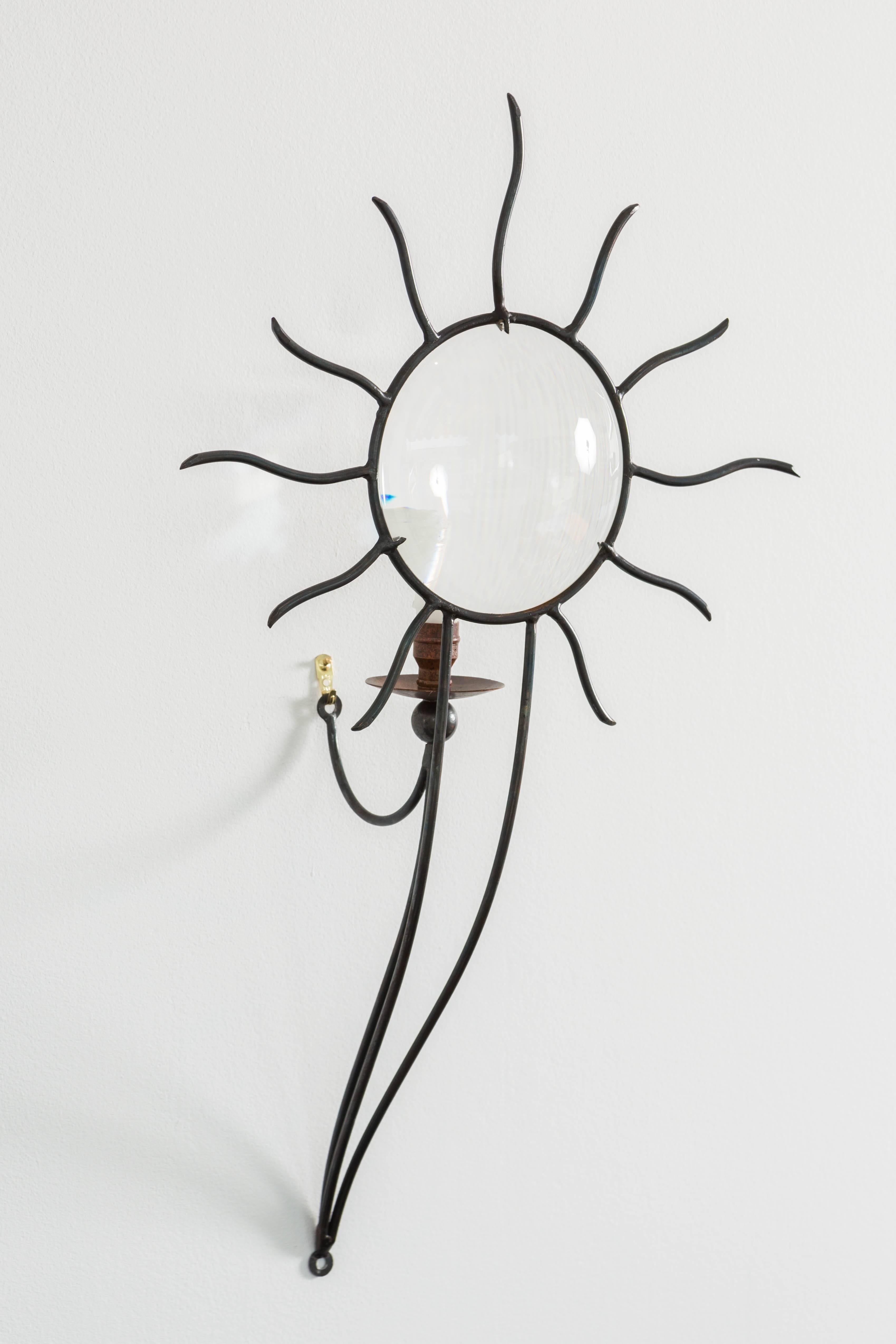 Late 20th century pair of thick-walled magnifying glass sconces in wrought iron forming a sunburst with brass socket and bobeche mounted on three supporting rods.`
Designed 1992 by André Dubreuil (1951, French).