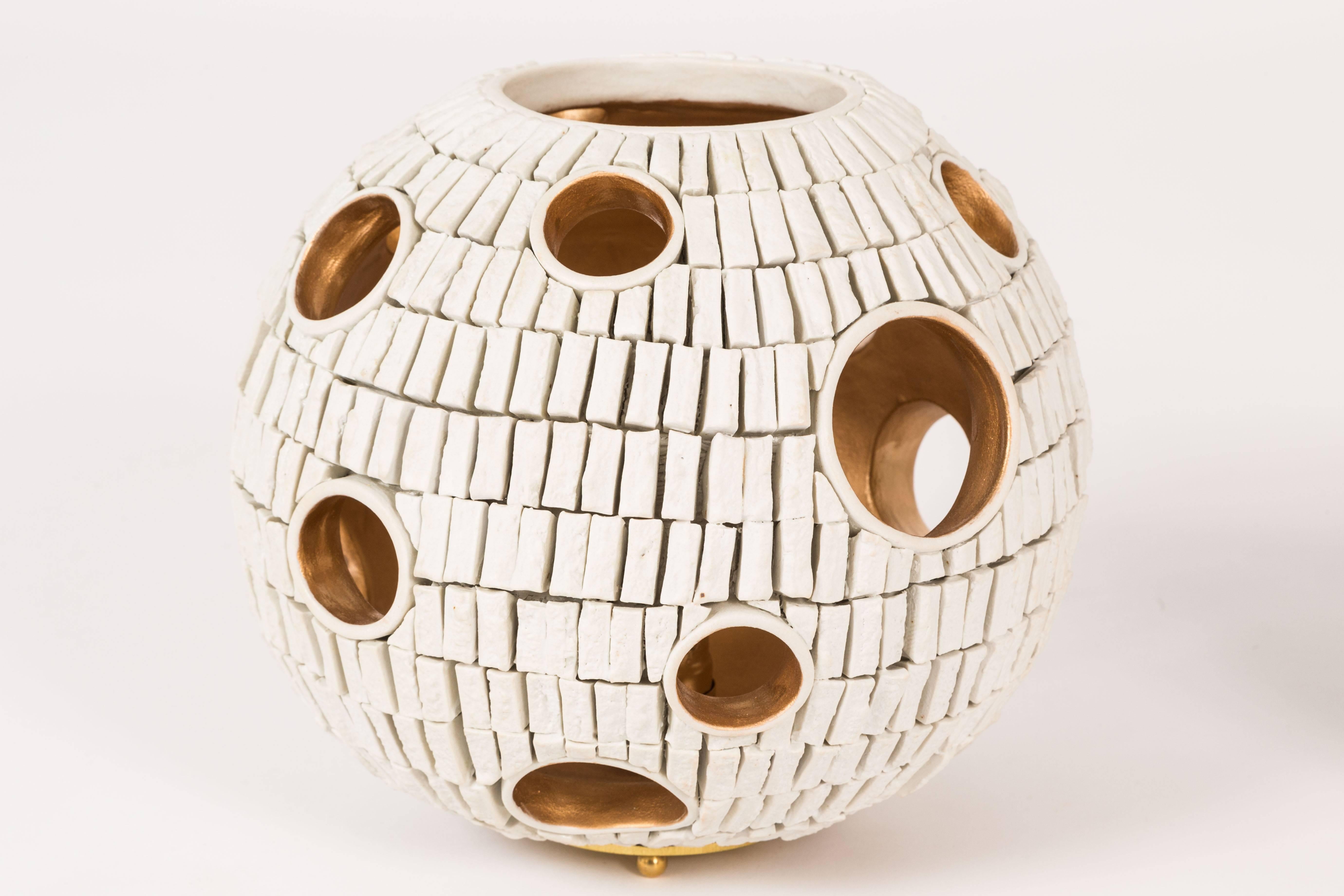 This is our latest collaboration with LA Ceramicist Titia Esties. Completely hand built this orb has an otherworldly feel to it. Assembled from hundreds of hand-cut tiles the varying sized cut-out allow for the glow of the gold painted interiors to