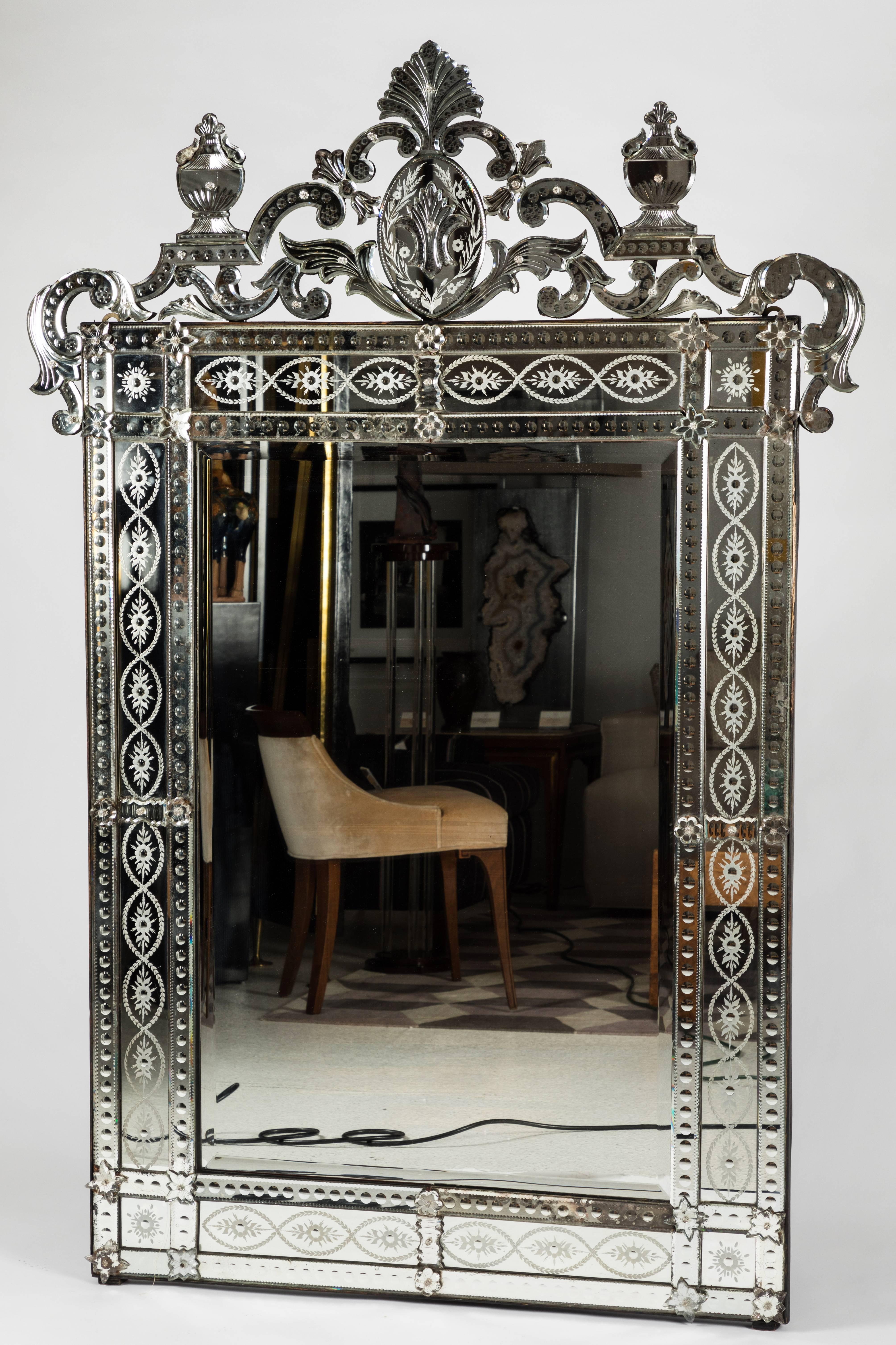 Beautiful Venetian mirror with lovely detail. The mirror frame features both carved and etched details with mirror overlays. The fanciful pediment features a cartouche with a pair of urns flanking the sides. The mirror is in very good original