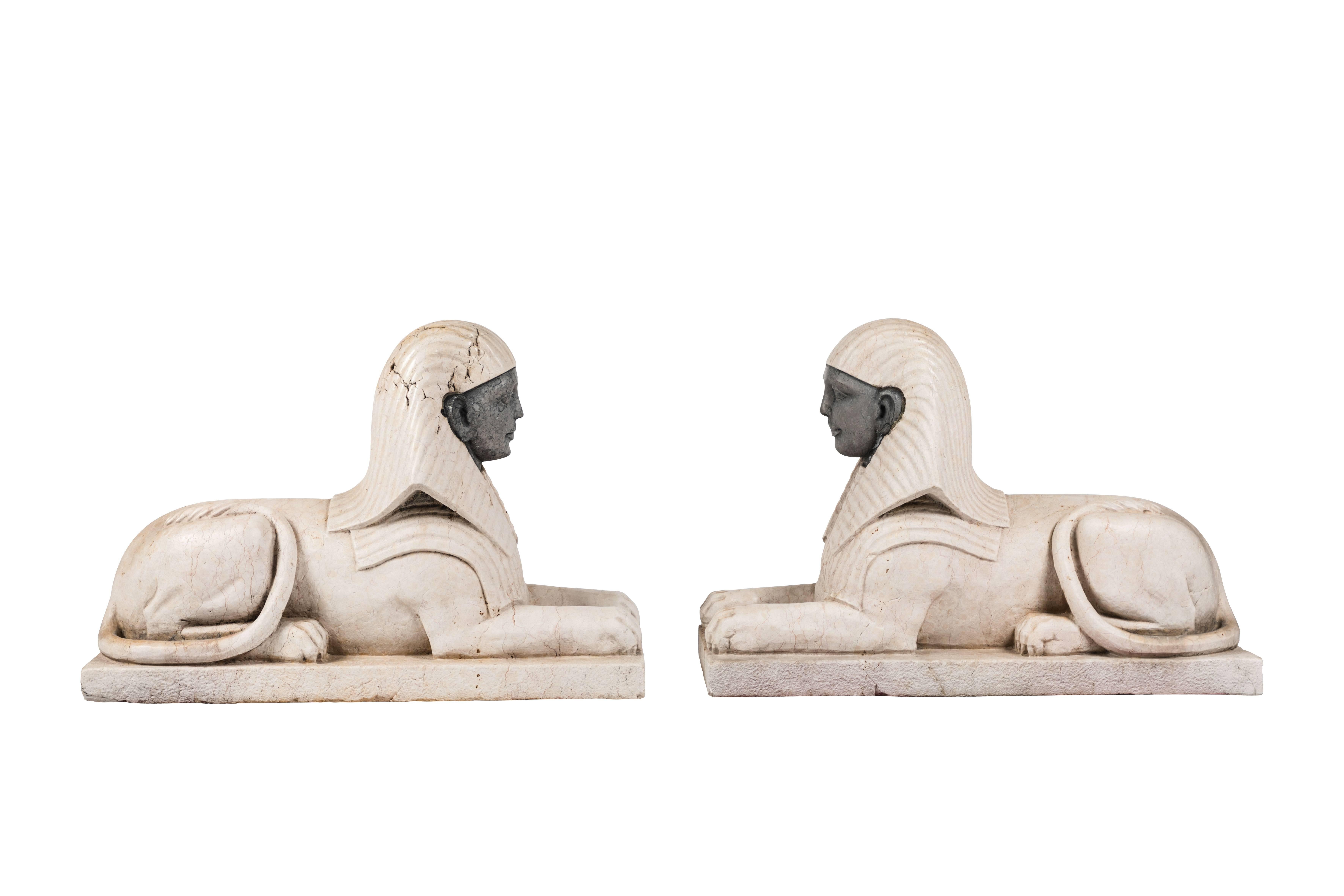 Amazing pair of multi stone Art Deco inspired Sphinxes.  Sitting proudly on a small plinth this classical form takes on a sleek 20th Century vibe.  Crema Marfil marble makes up the overall composition, while the faces are of a black/grey marble. 