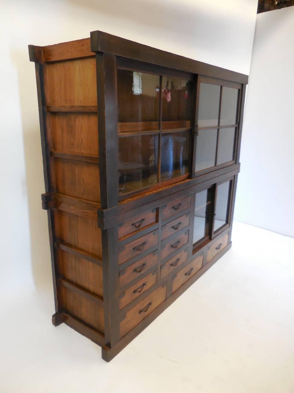 19th century shiop tansu cabinet with two sliding glass doors on top piece with one interior shelf. Original glass.
Bottom piece consists of eleven drawers and a smaller pair of sliding doors with an interior shelf.
Original hardware, bamboo nails.