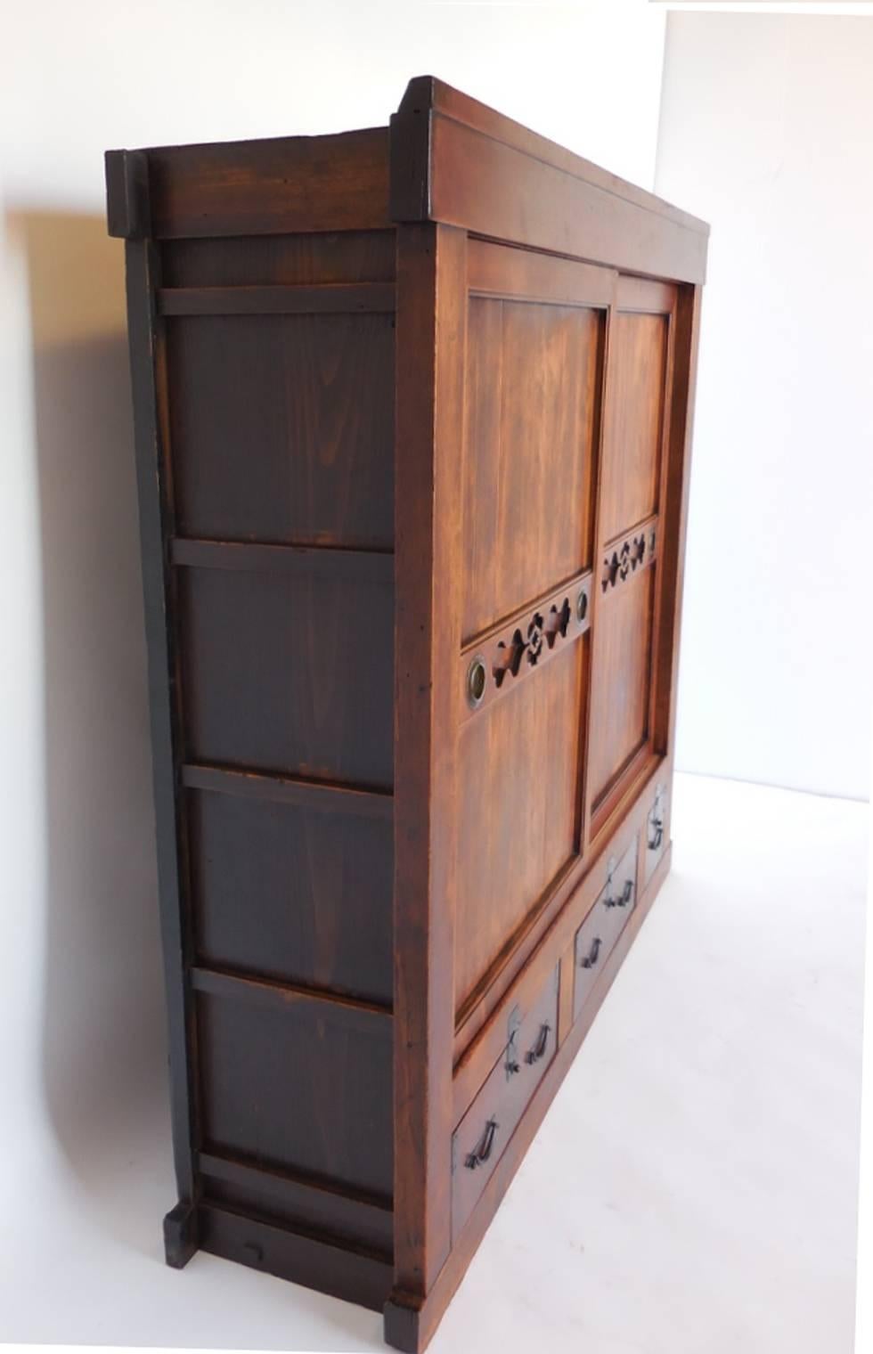 19th century Japanese tansu chest used for storing bedding. Cabinet has three drawers and a pair of sliding doors with decorative cutouts. Interior shelves. All original. Bamboo nails. Hinoki wood. Beautiful patina. Very functional.