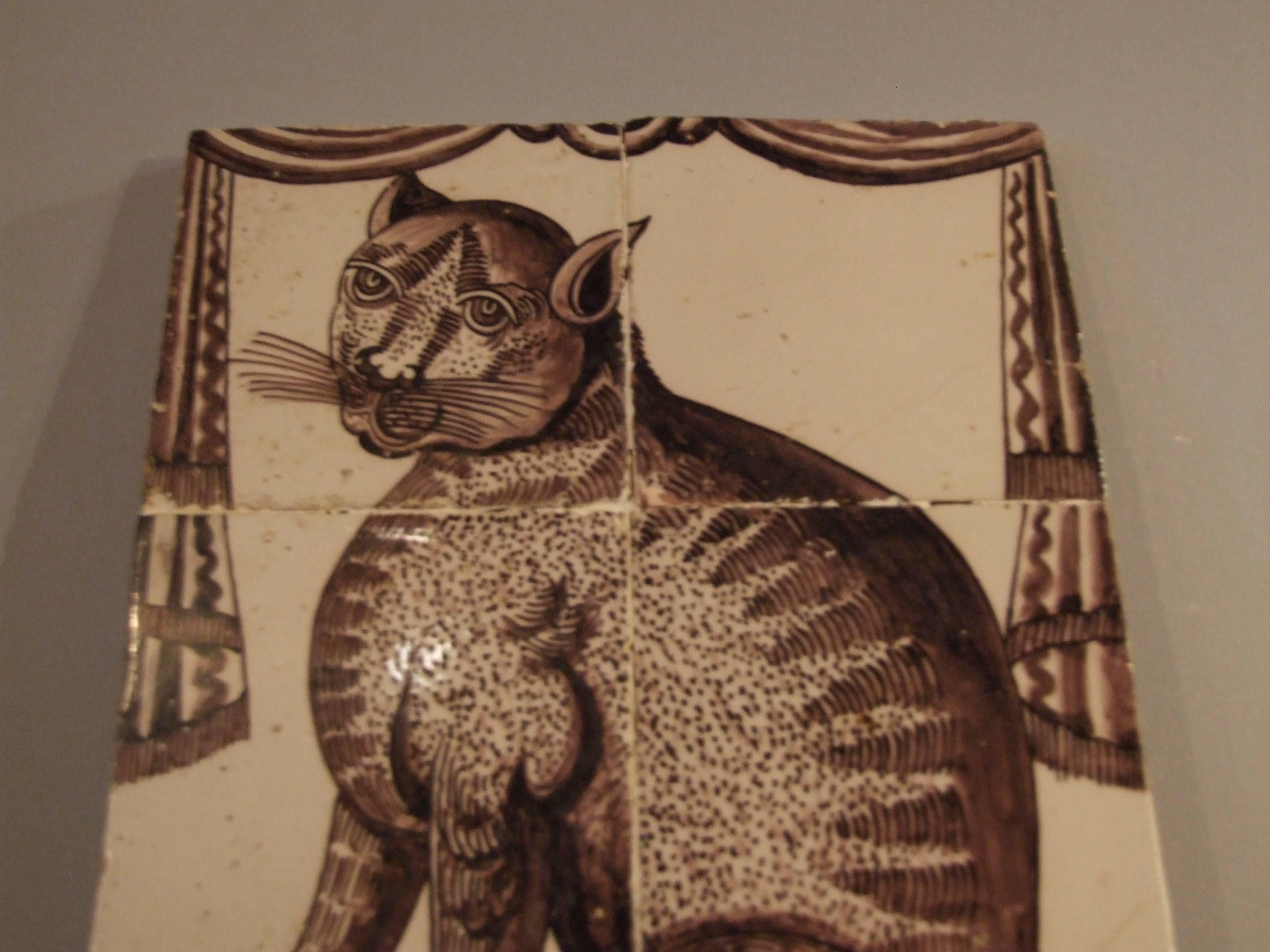 Unique and wonderful 18th Century delft tile picture of a two-tailed cat sitting on a tiled floor, framed by drapes.