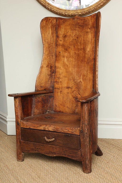 An exceptional example of an 18th century Welsh shepherd's chair with good, nutty color in richly patinated sycamore having boarded back and scalloped wings with flattened curved oak arms, one with the remnants of a candleholder, deeply saddled